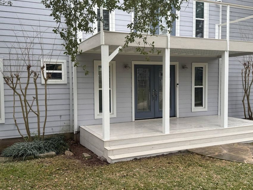 A light gray two-story house with a wooden porch, double doors, and a balcony. A light gray two-story house with a wooden porch, double doors, and a balcony.