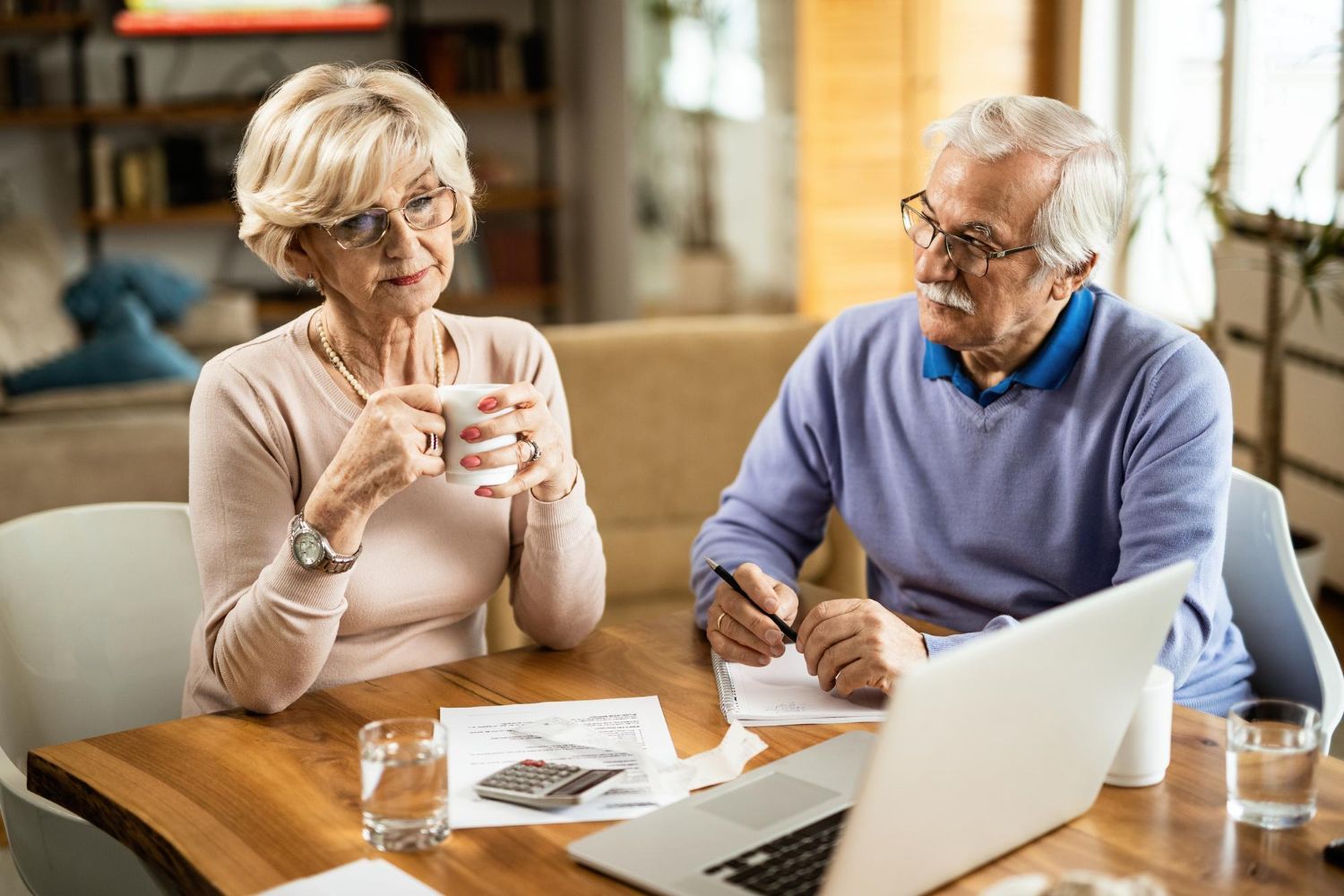 Older couple reviewing documents at a table with a laptop, drinks, and pen.