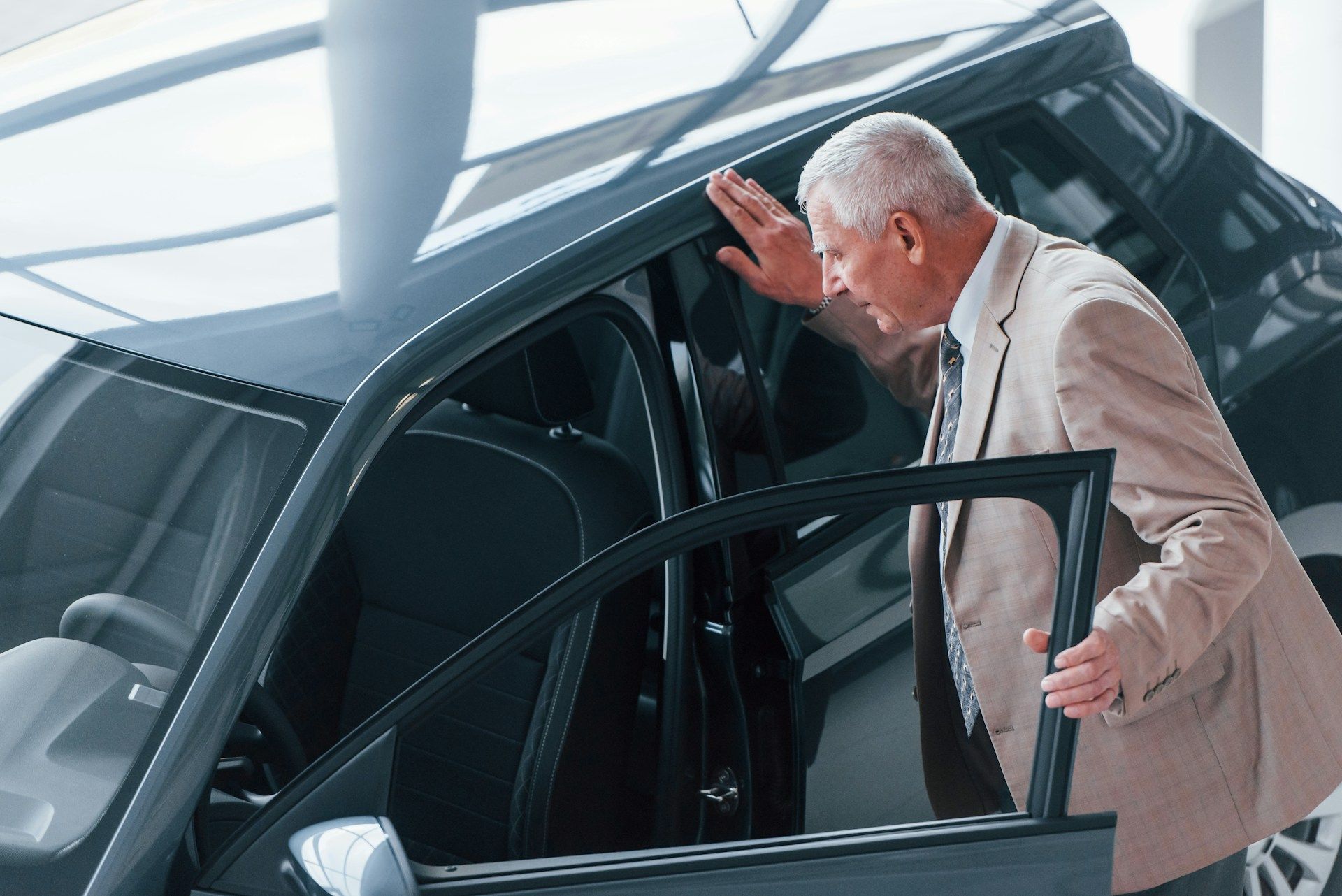 Man examining the interior of a black car in a showroom, looking inside.