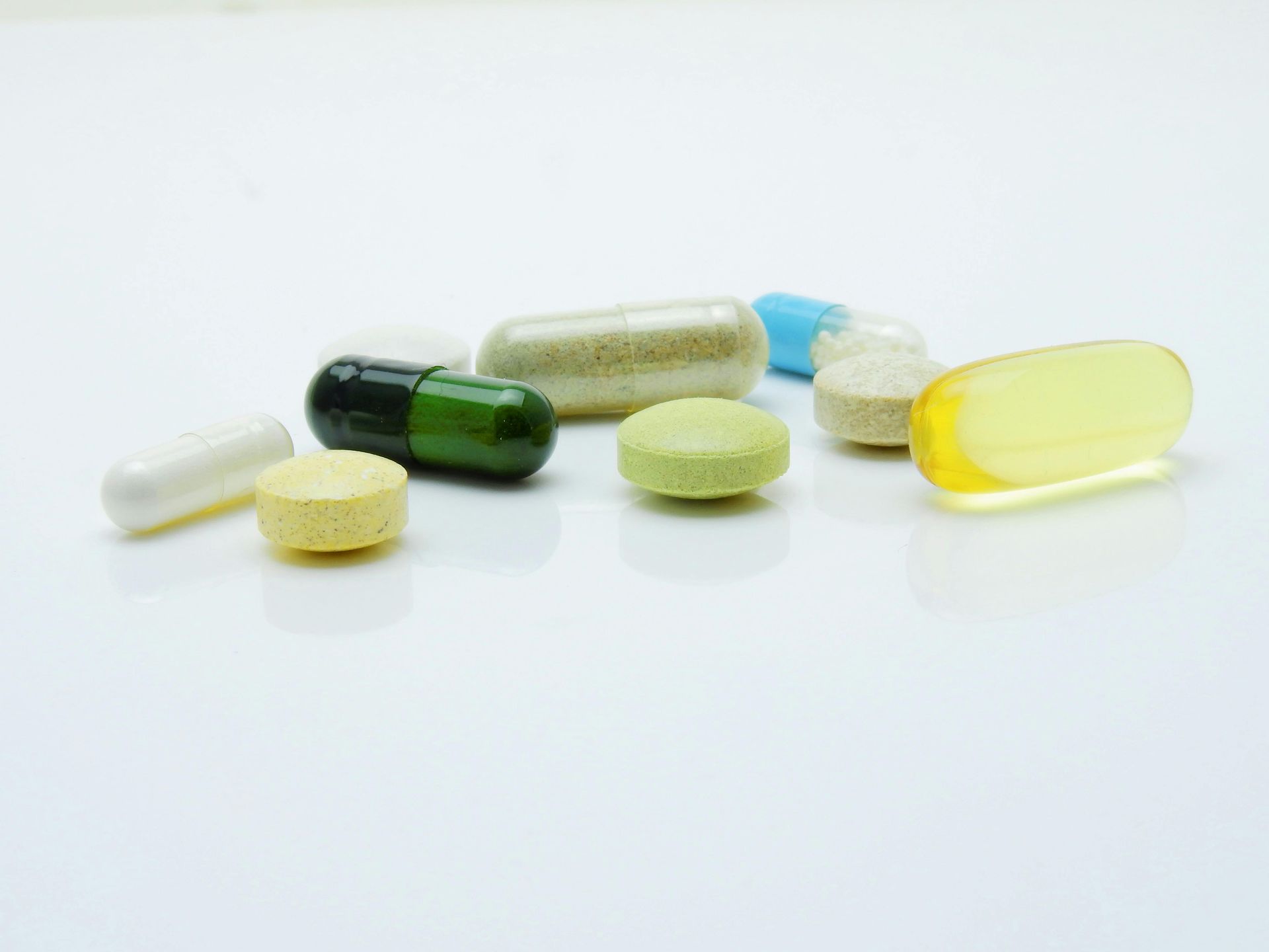 Assorted pills and capsules in various colors on a white surface.