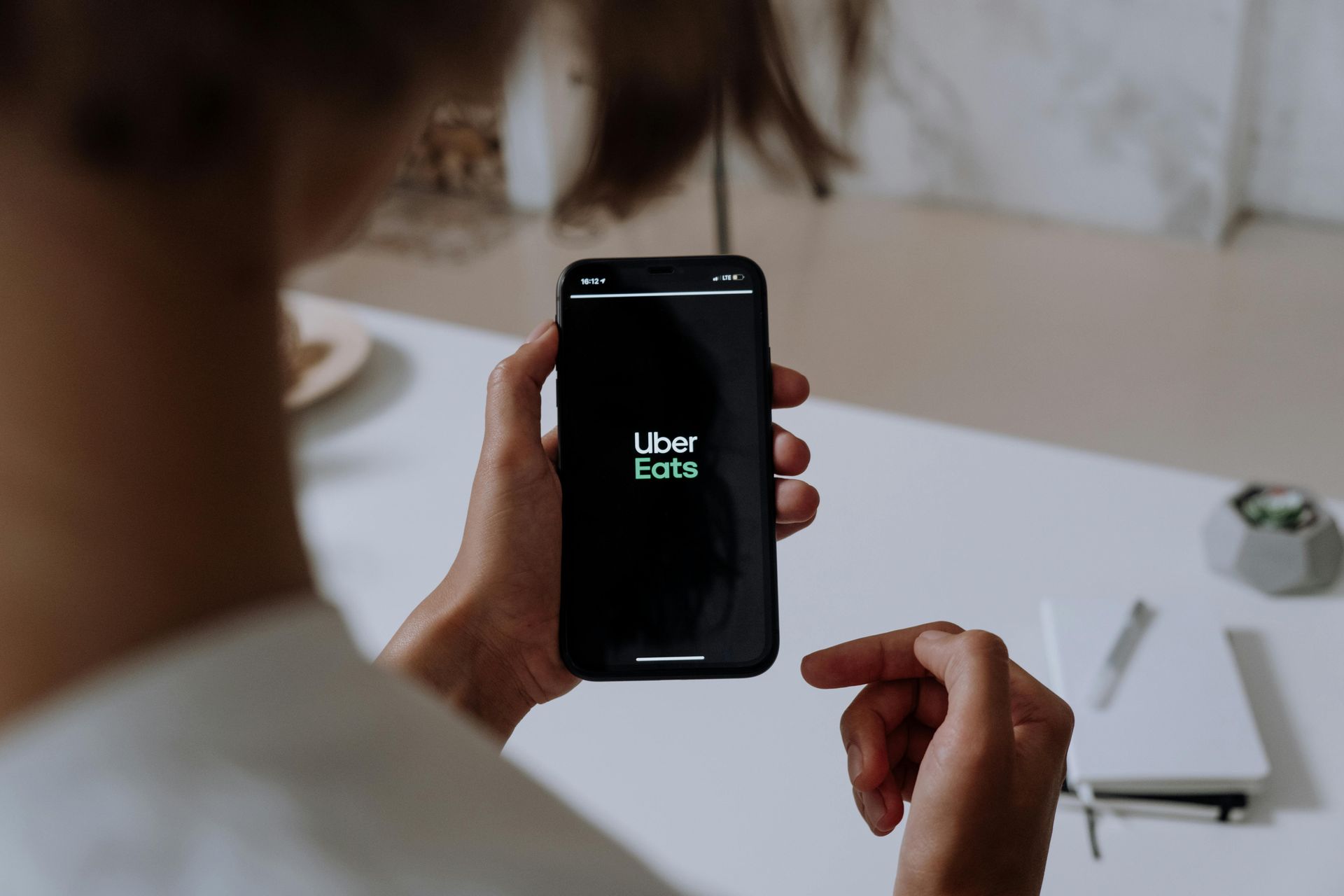 Person holding a phone with the Uber Eats app open, indoors at a desk.