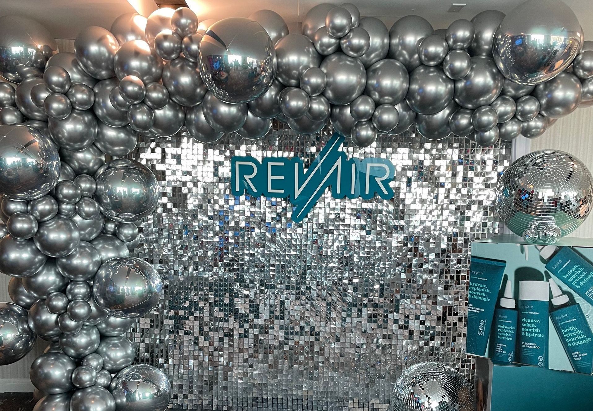 Metallic silver chrome balloon wall over sequin backdrop with branded corporate logo display