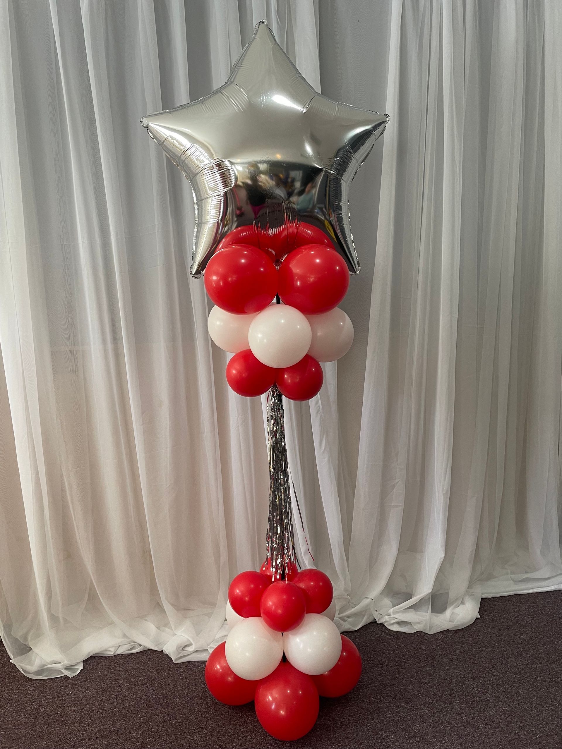 Silver star foil balloon topper on red and white balloon column for an indoor event