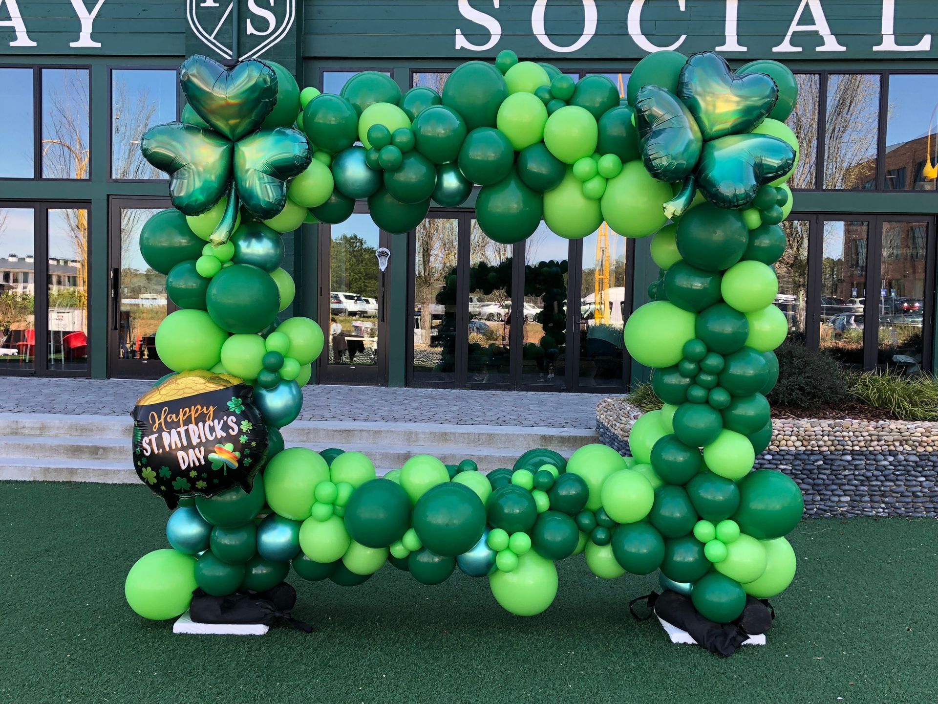 Green organic balloon arch framing outdoor entrance for St Patrick’s Day or themed celebration