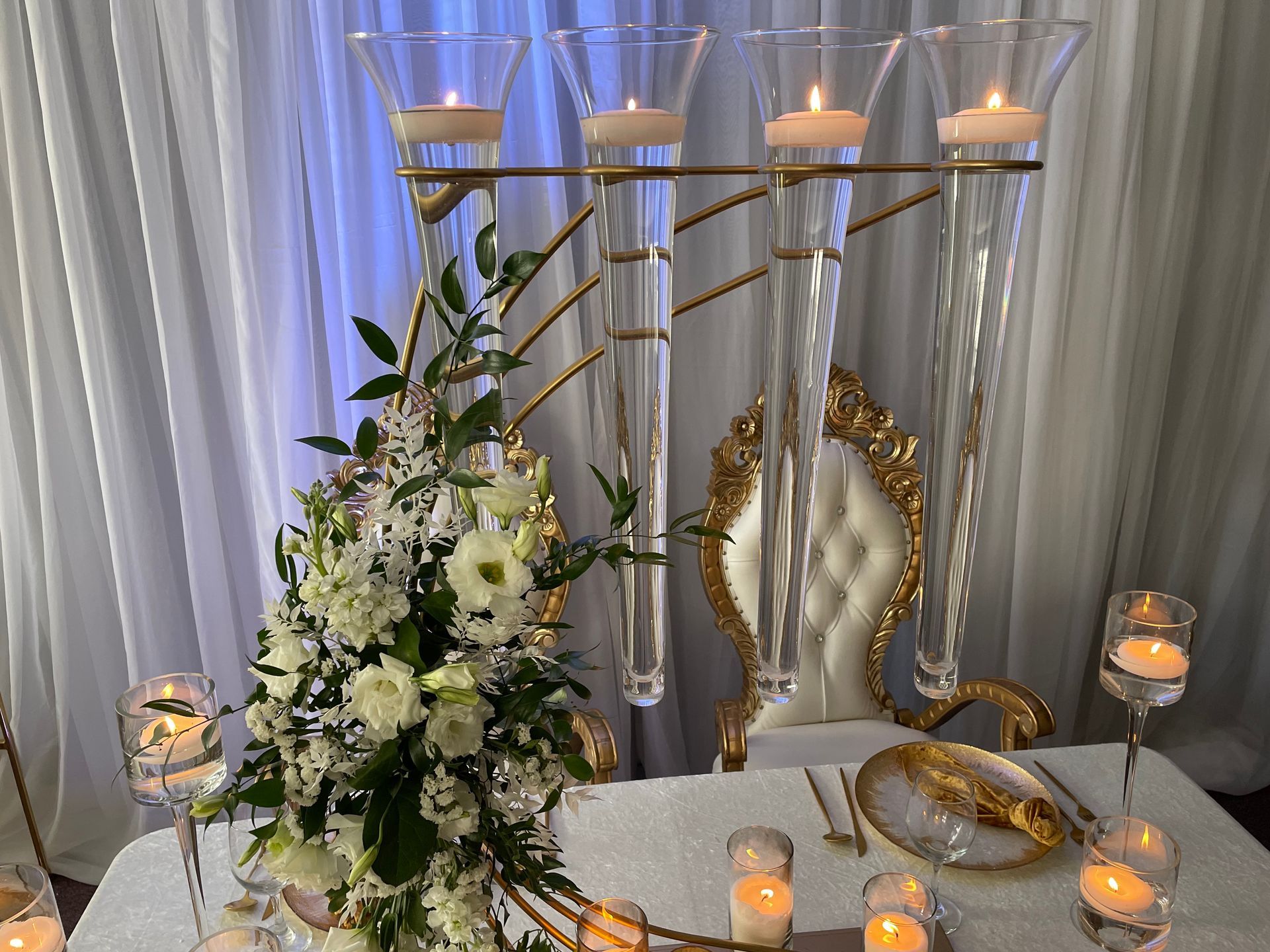 Tall glass candle holders with white florals and greenery on a decorated event table