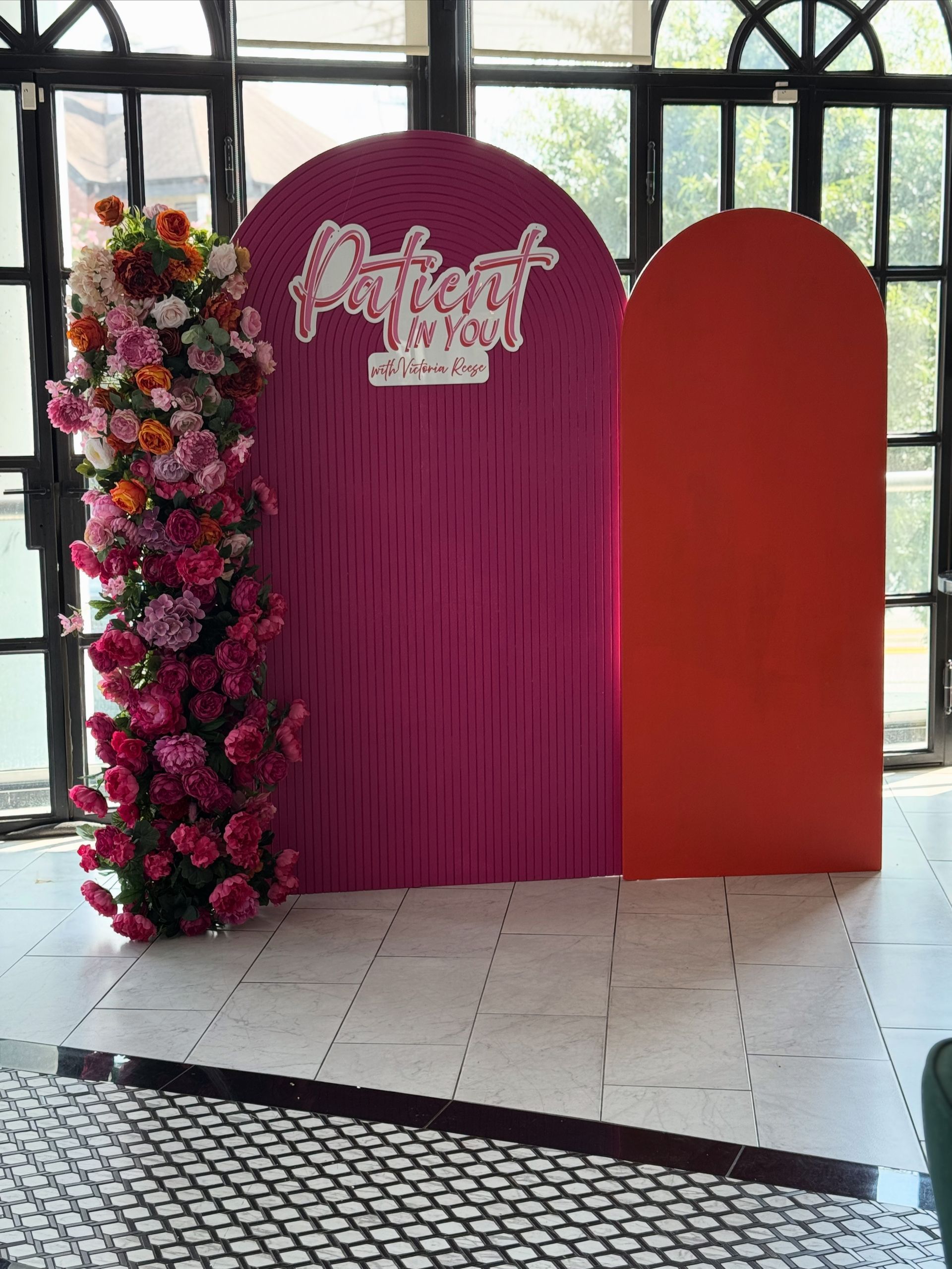 Pink arched statement backdrop with floral installation and custom “Patient in Pink” event signage for celebration photos