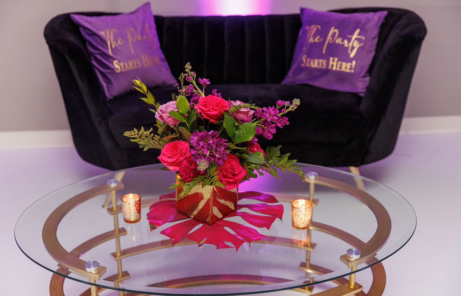 Lounge seating setup with black velvet sofa, themed pillows, floral centerpiece, and candles for party or reception décor