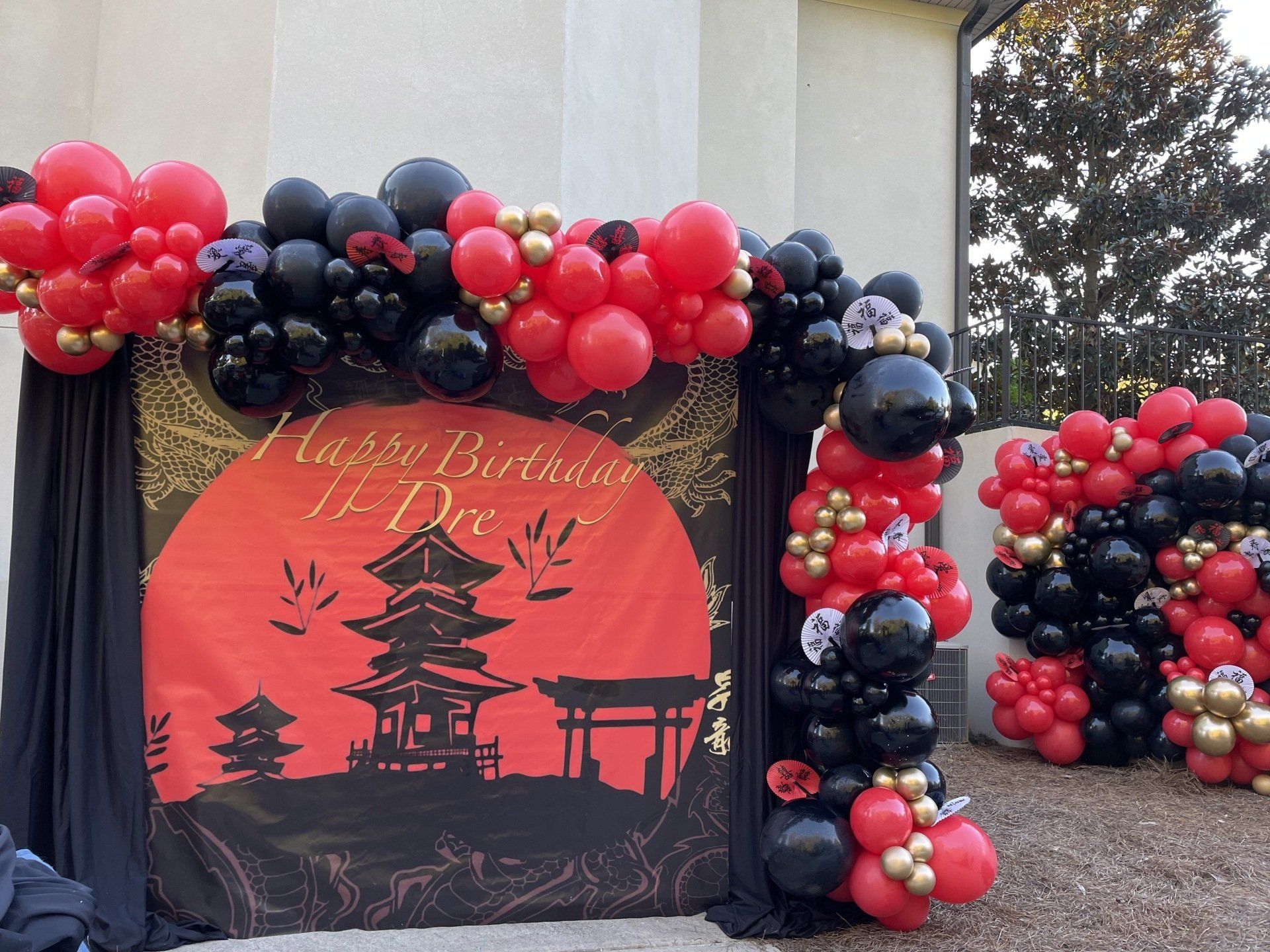 Asian inspired birthday backdrop with red black and gold balloon garland and custom round sign