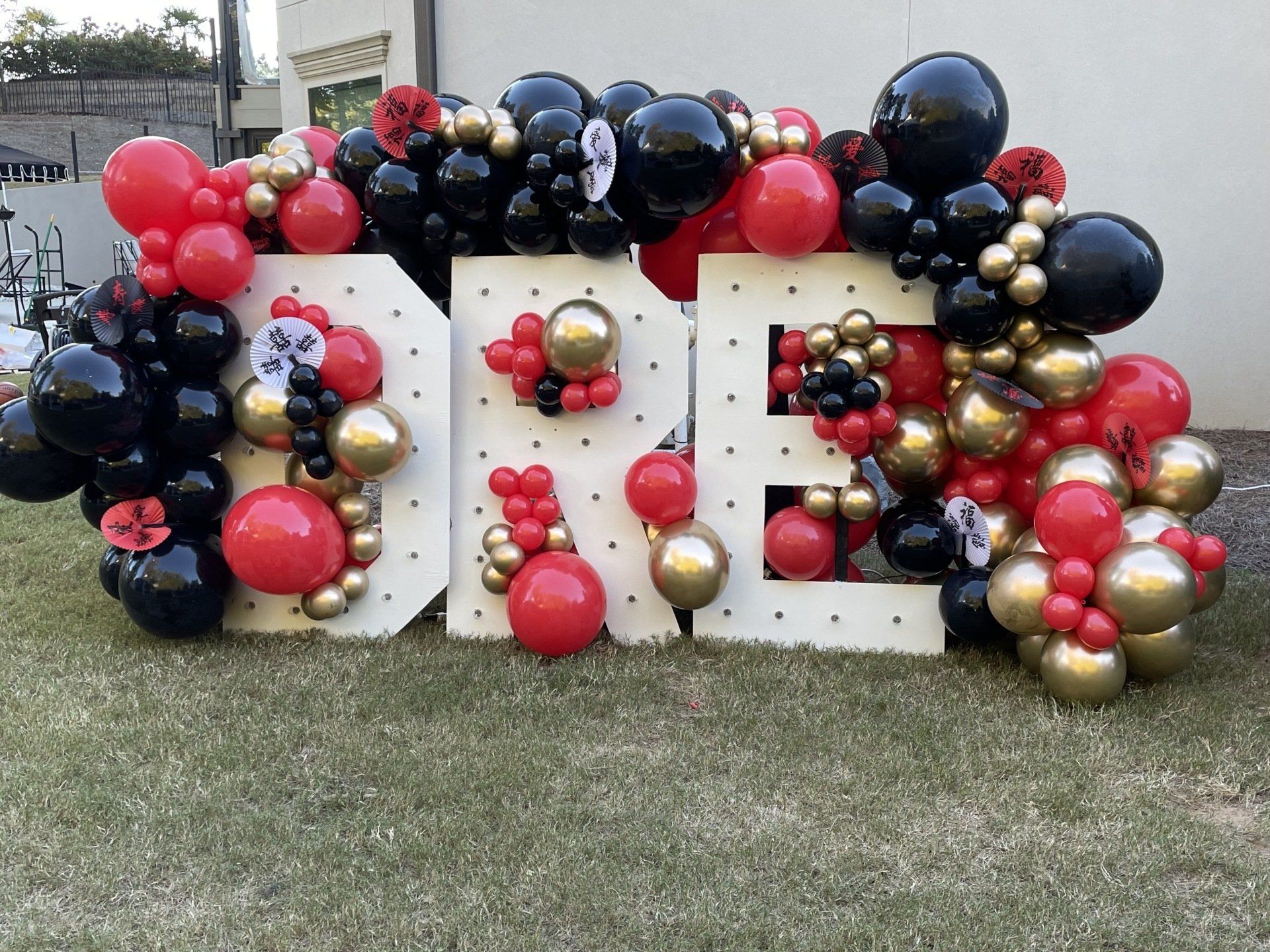 Red black and gold balloon wall with large marquee numbers for bold milestone birthday party