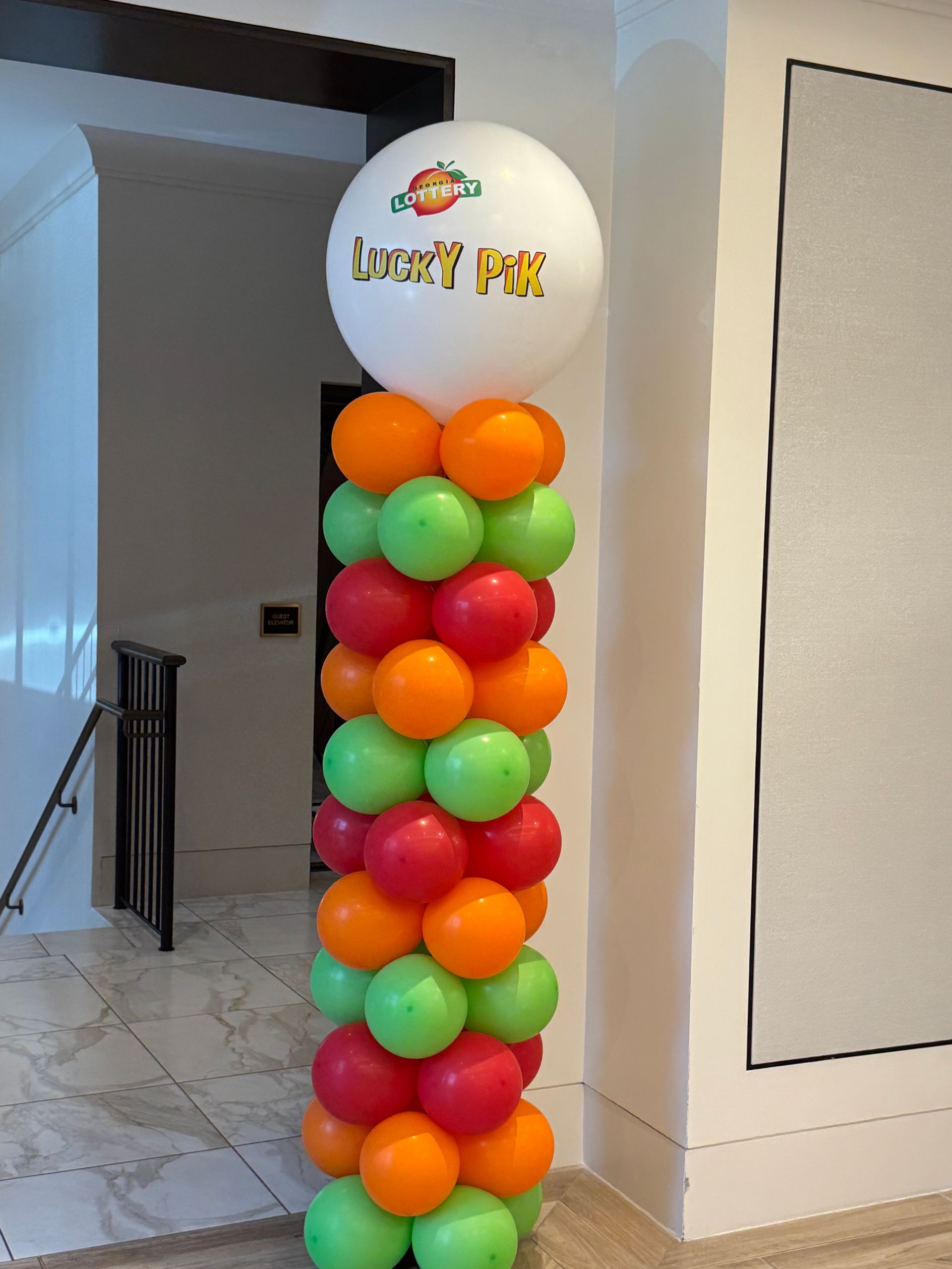 Colorful balloon column with large branded “Lucky Pik” topper balloon for an indoor event