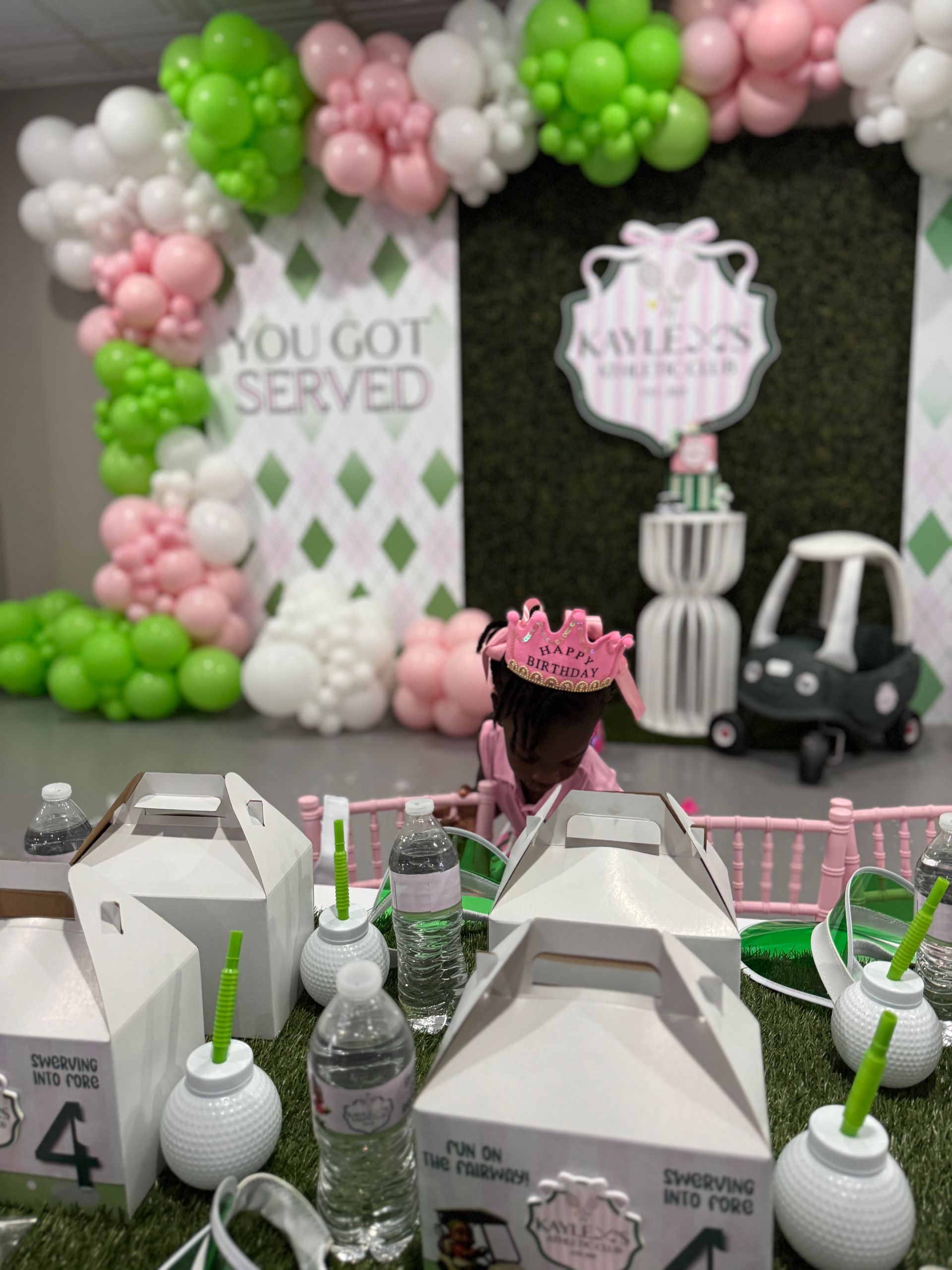 Pink white and green balloon garland framing custom party backdrop with personalized sign