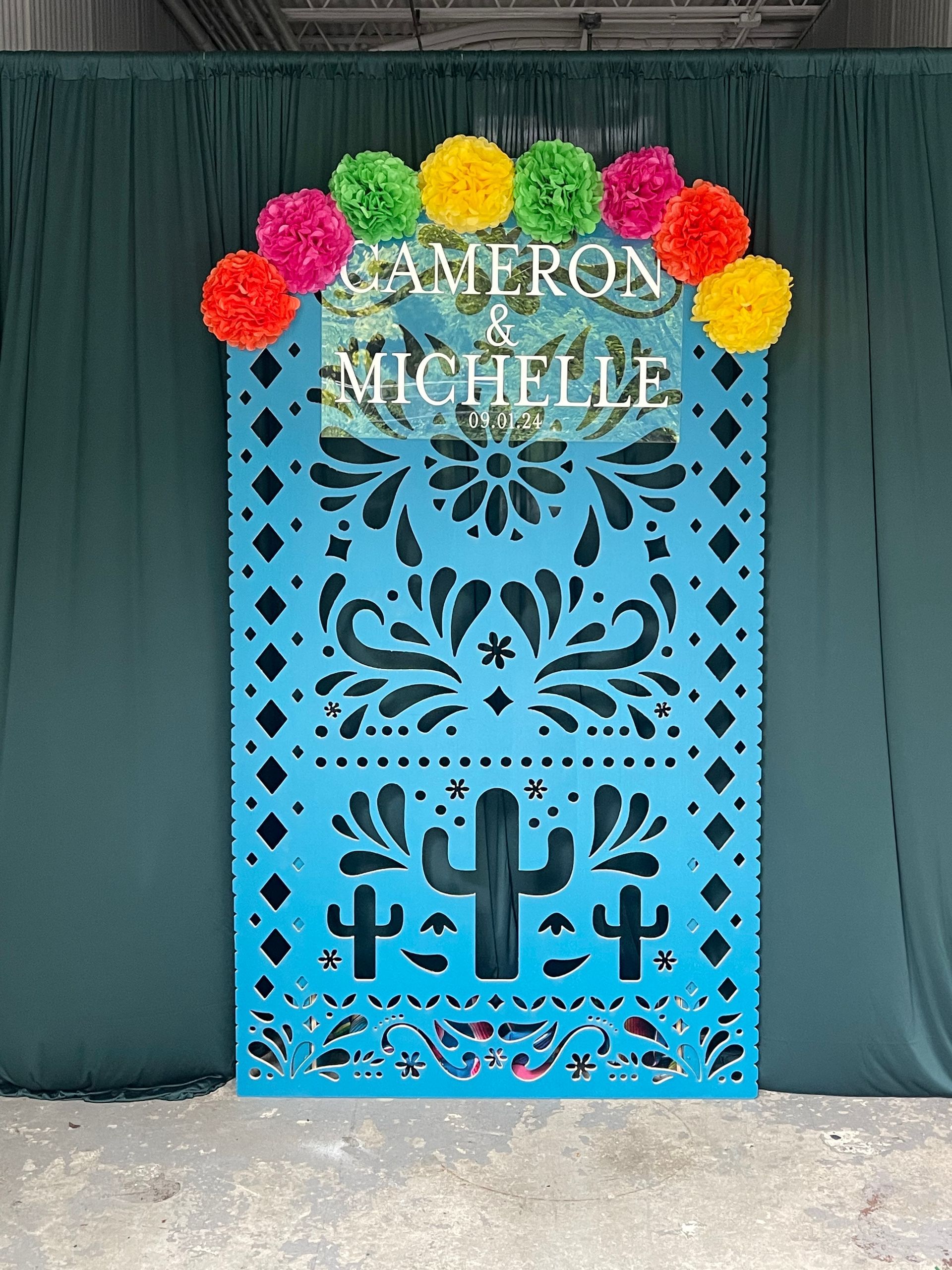 Custom name backdrop with teal panel and colorful paper flowers for wedding or celebration photo area