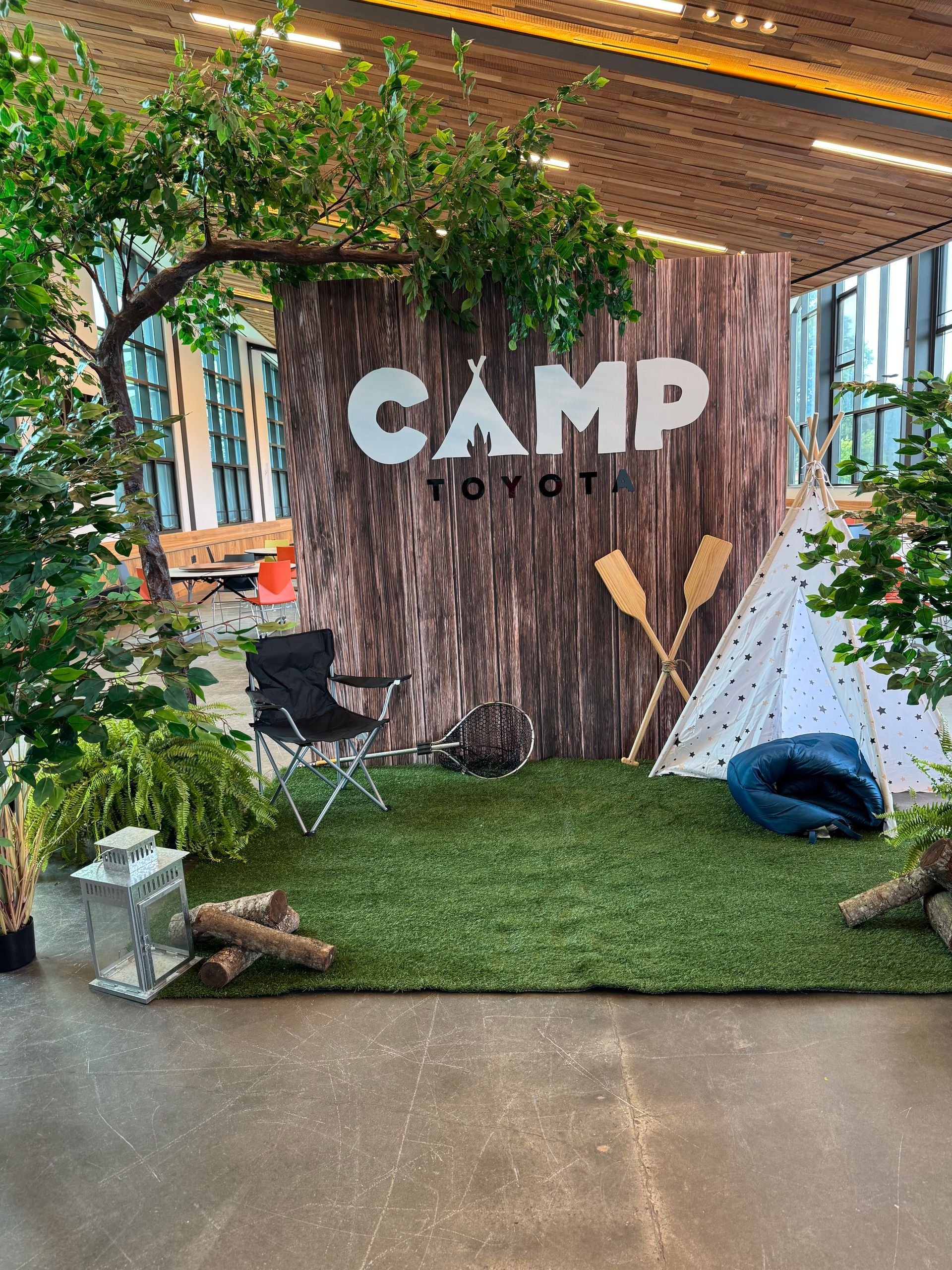 Indoor woodland themed backdrop with artificial trees and “Camp Toyota” signage for corporate or camp style event display