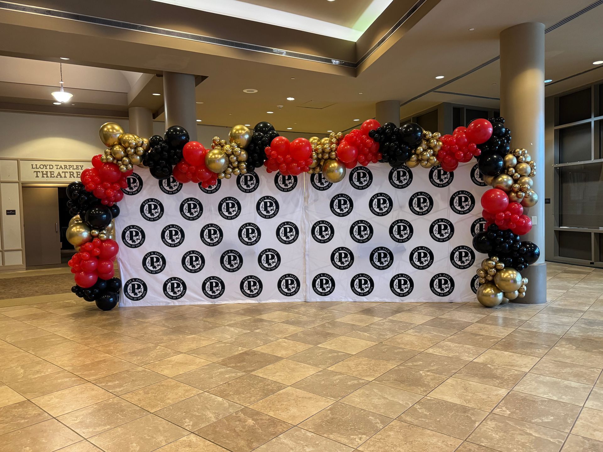 Long branded step and repeat wall with red black and gold balloon garland for corporate or school celebration