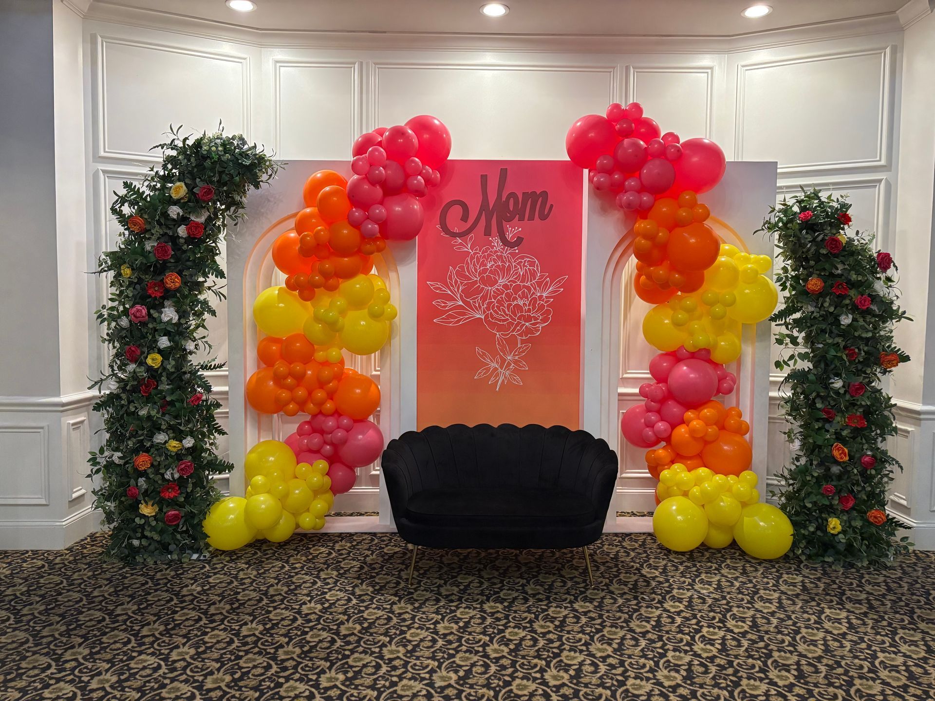 Rainbow balloon arch framing a decorative backdrop and lounge seating for an indoor event