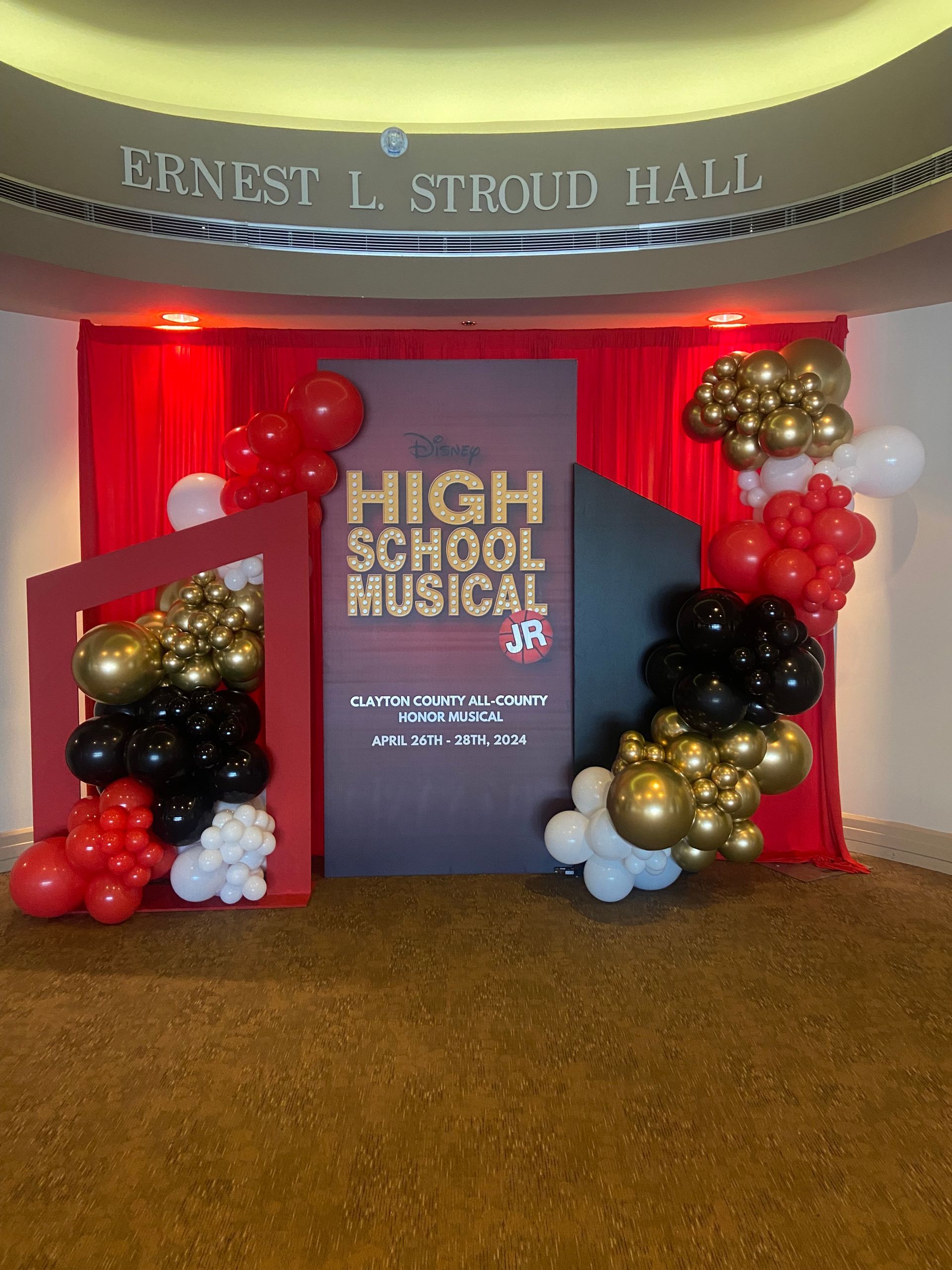 Red gold and white balloon decor framing stage backdrop for school or themed event display