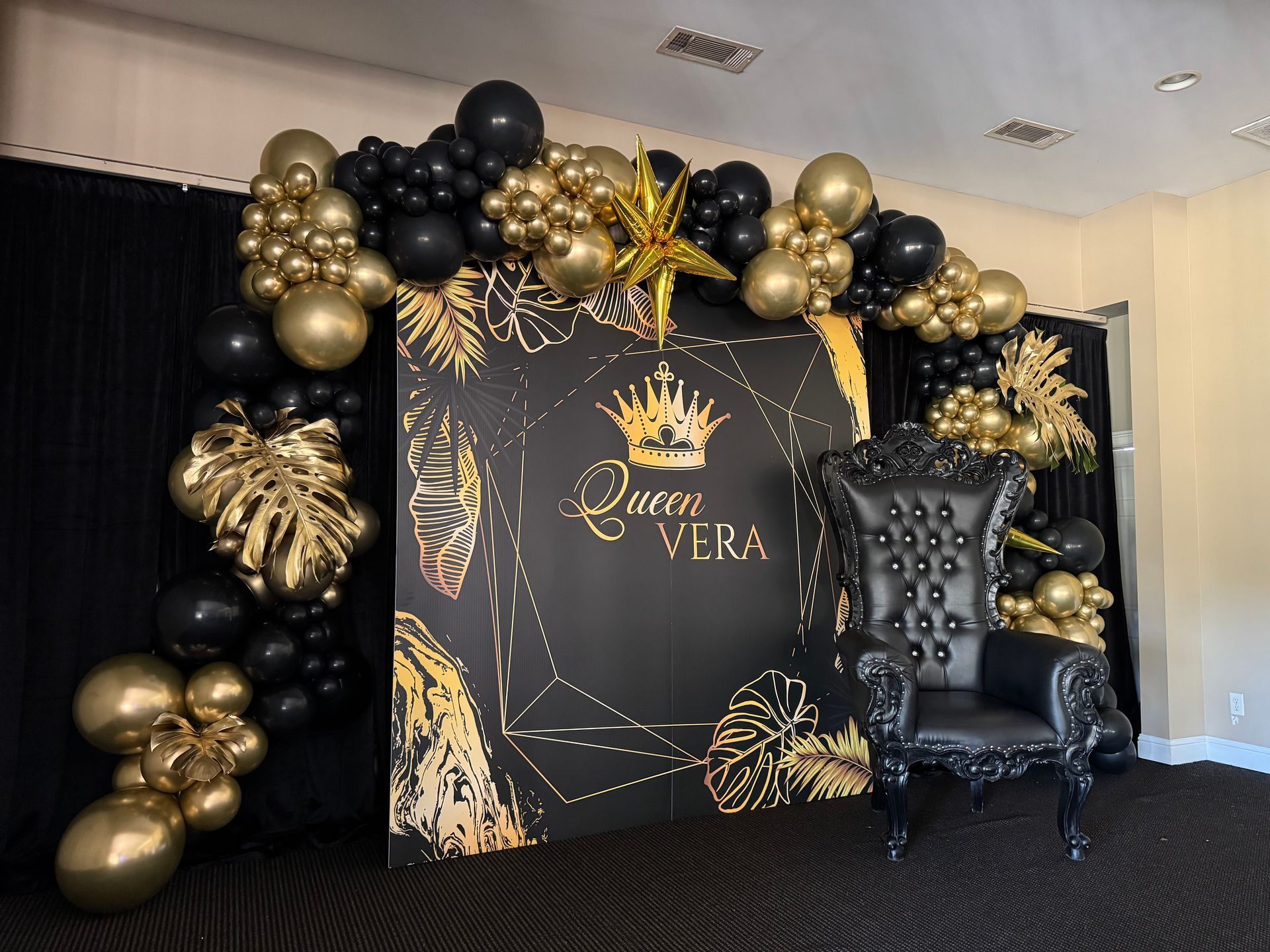 Black and gold luxury throne chair backdrop with balloon garland and custom name sign for elegant birthday or milestone party