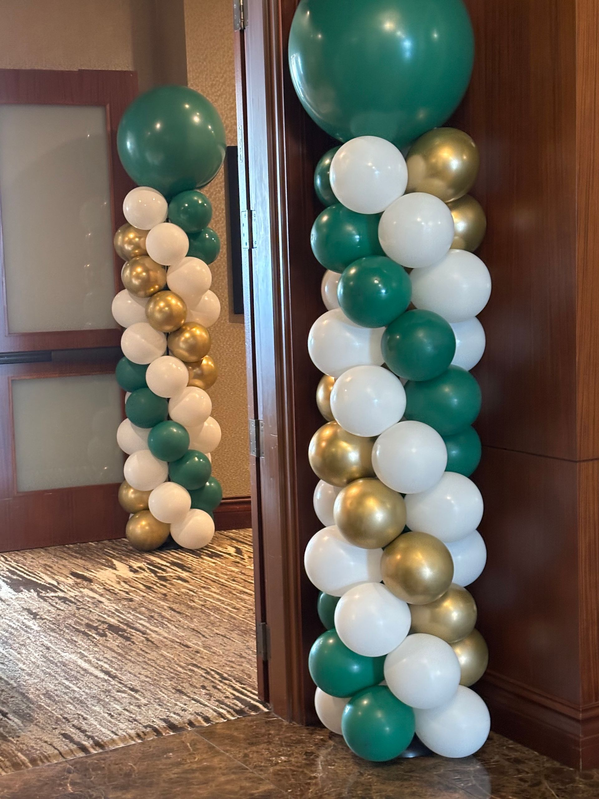 Green, white, and gold balloon column décor set beside an indoor doorway entrance
