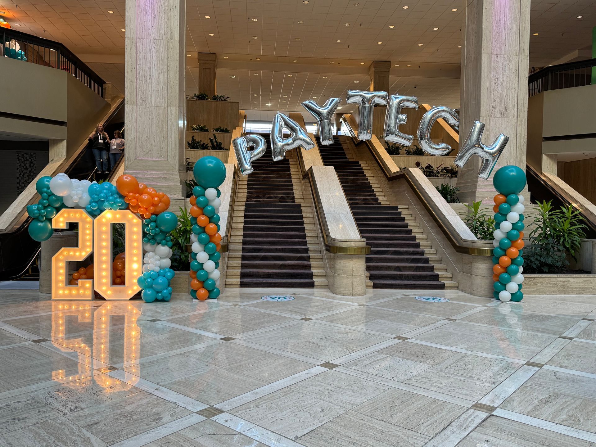 Balloon décor installation with silver PAC-TECH letters and number 20 display at an indoor event venue staircase
