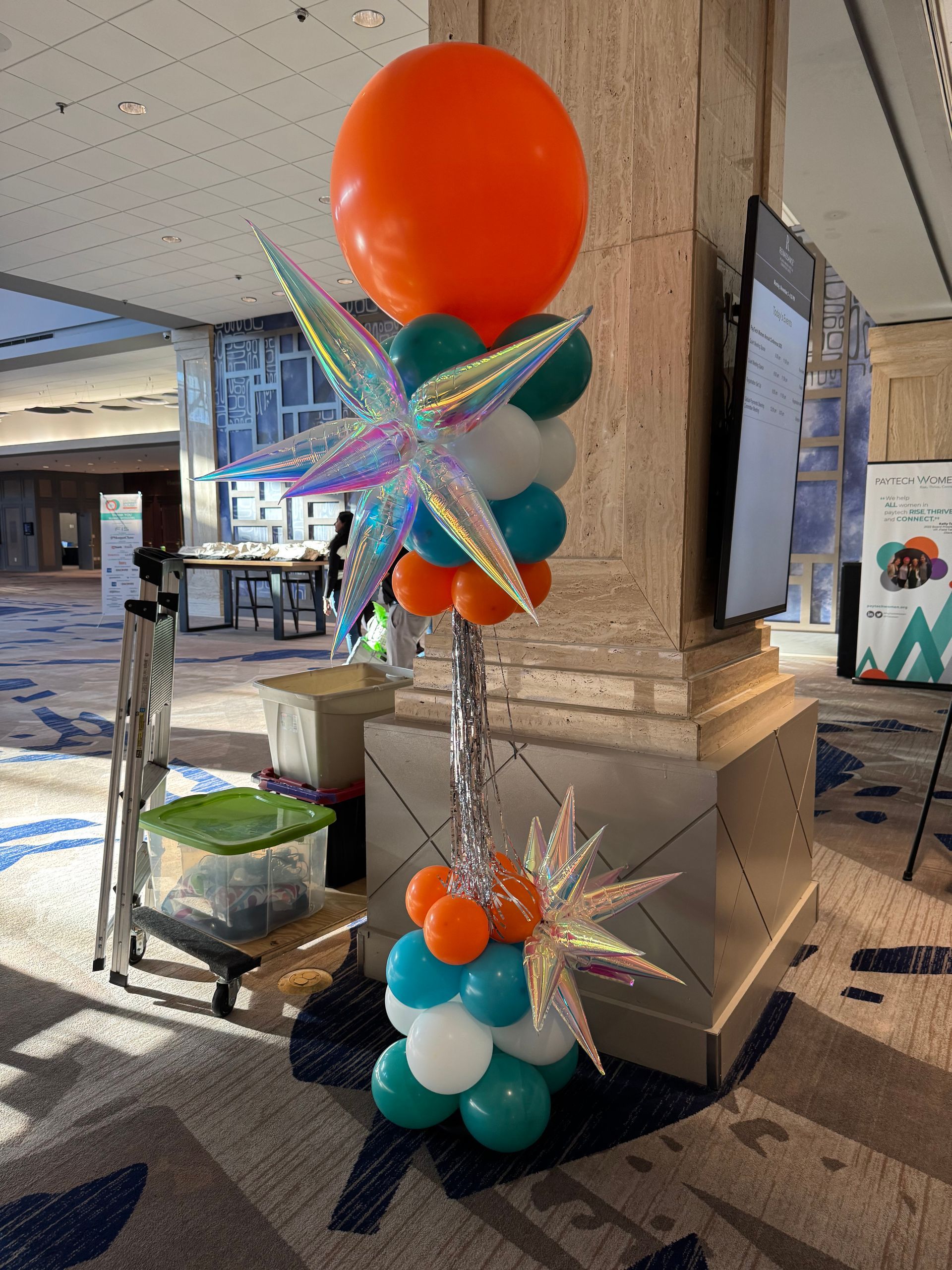 Orange and teal balloon column with iridescent star topper for an indoor event display