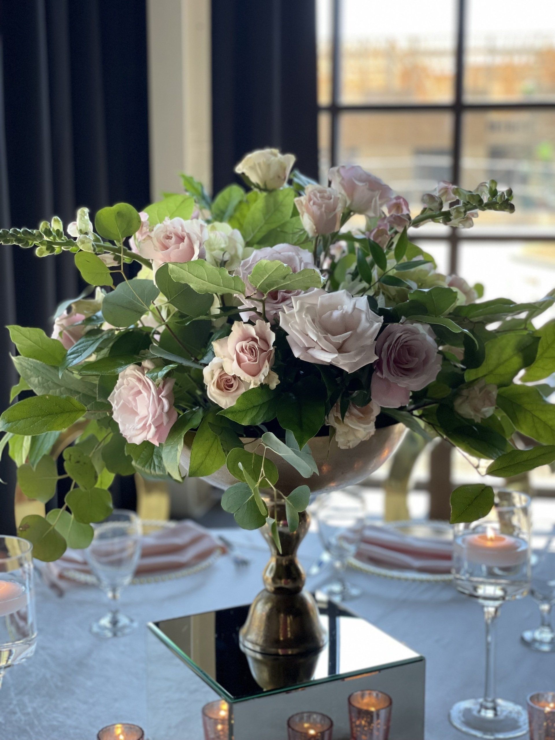 Soft pink and white floral arrangement with greenery placed near a window indoors