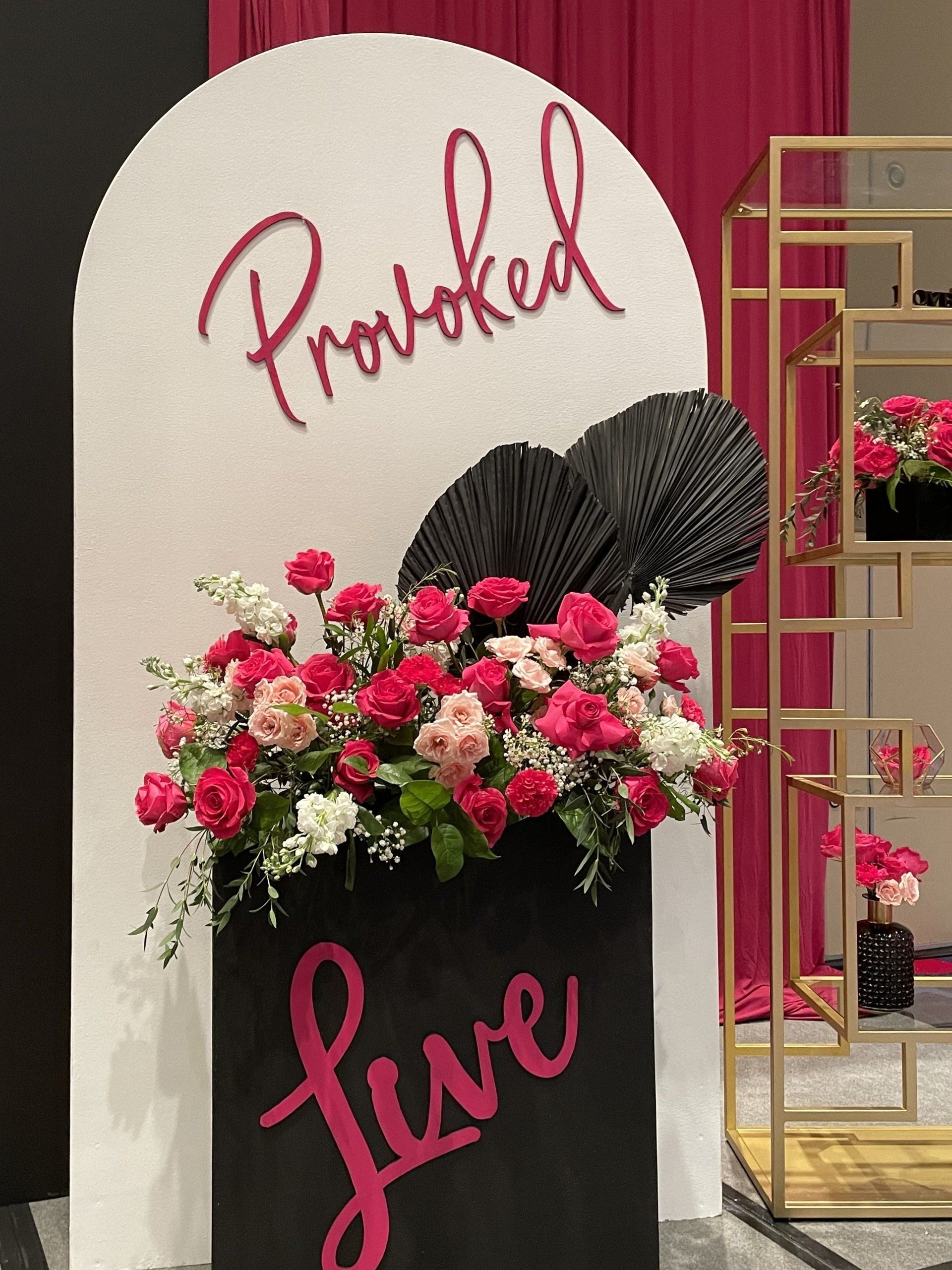 Curved event backdrop with Provoked sign, gold shelving, and pink floral accents