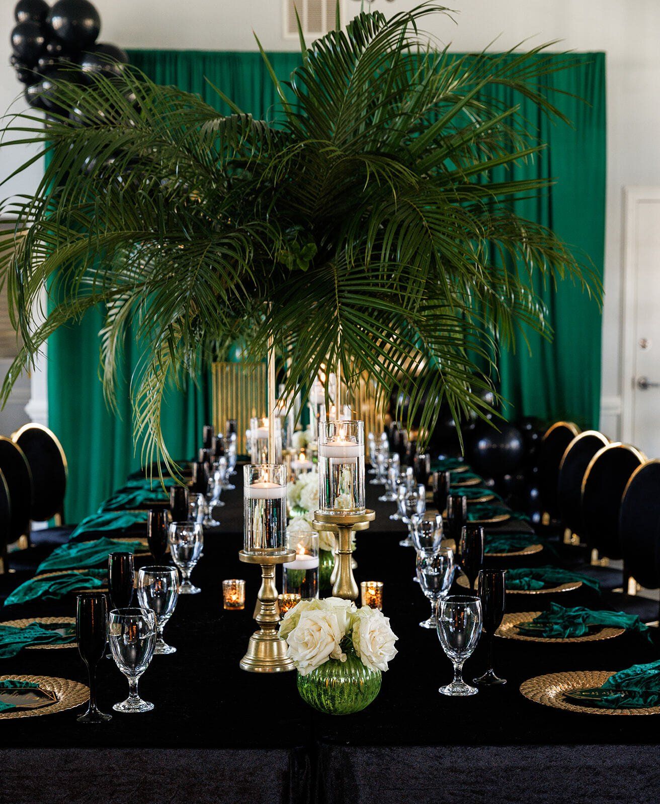Lush green palm arrangement used as décor against a green draped backdrop