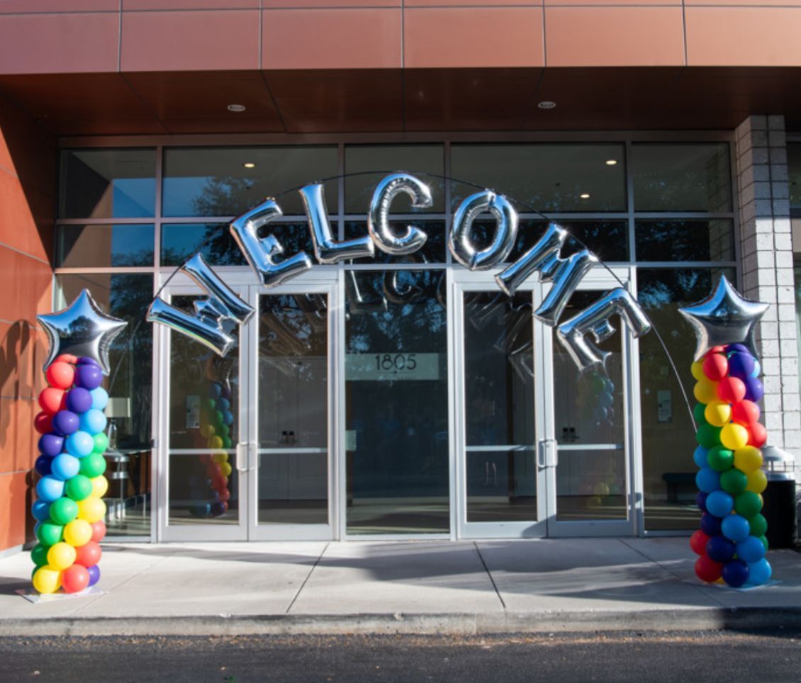 Rainbow balloon arch entrance outside a building with welcome balloon lettering