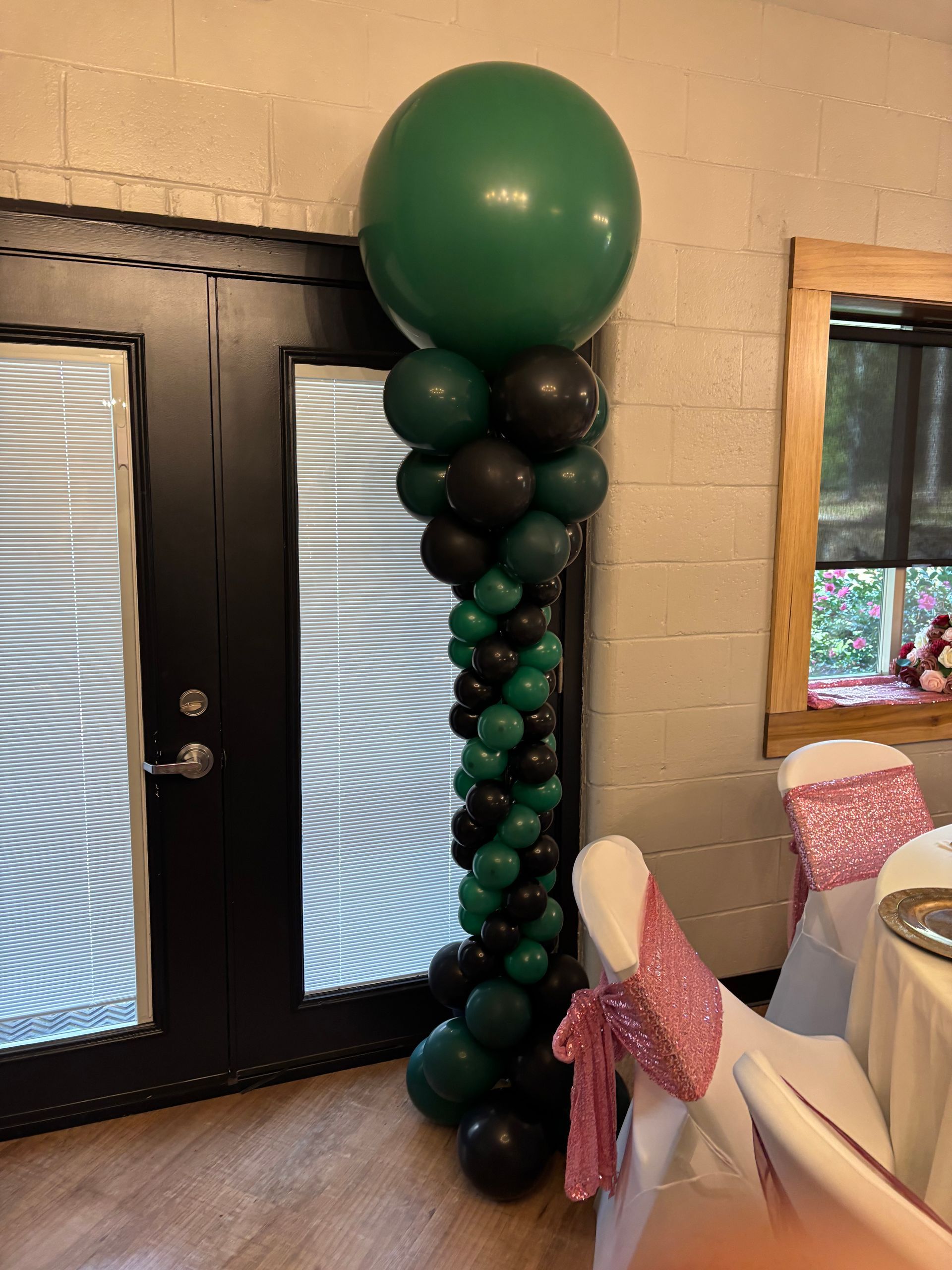 Green and black balloon column with oversized green topper balloon beside an indoor doorway