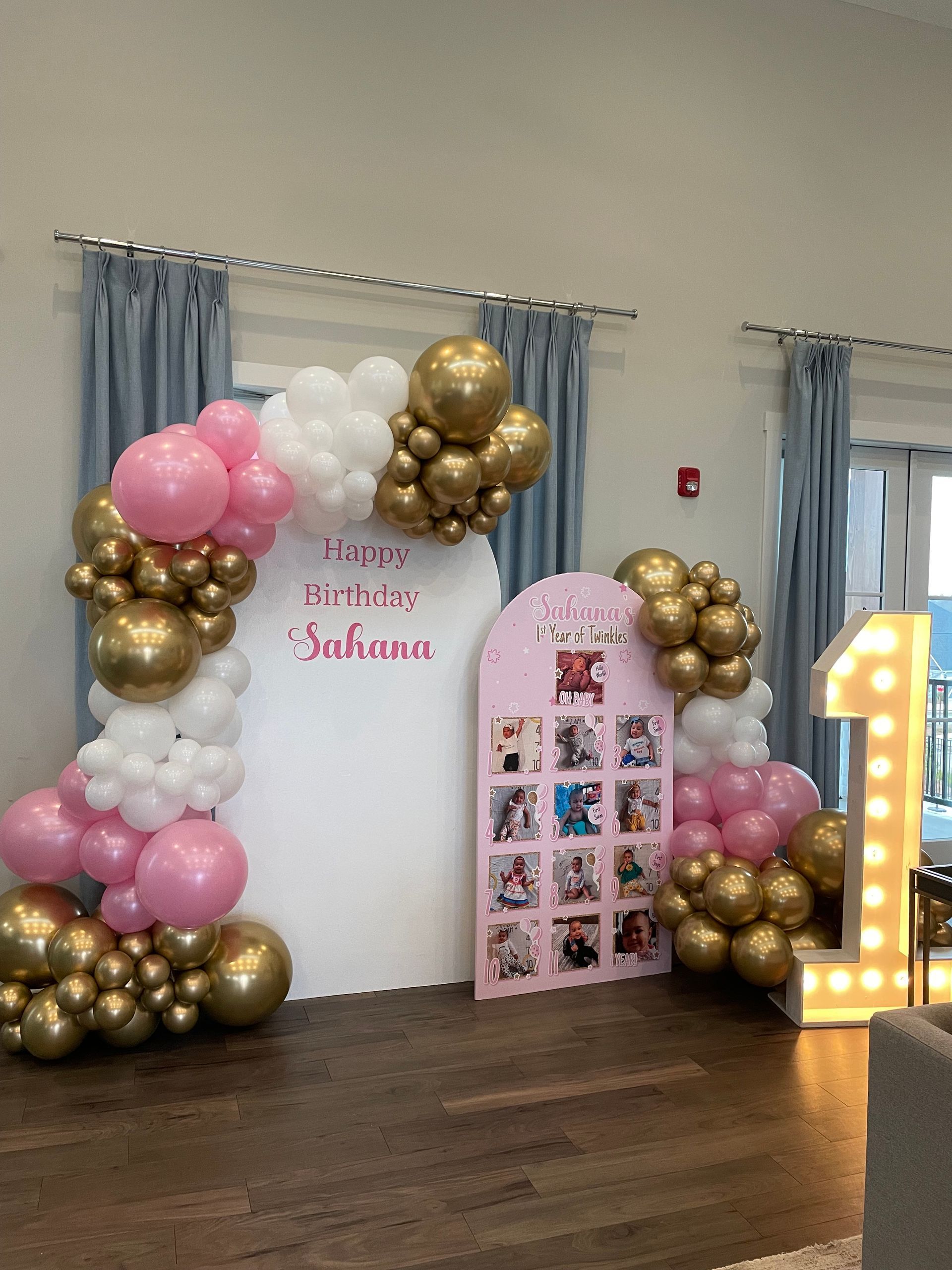 Pink white and gold balloon garland framing birthday backdrop inside event space