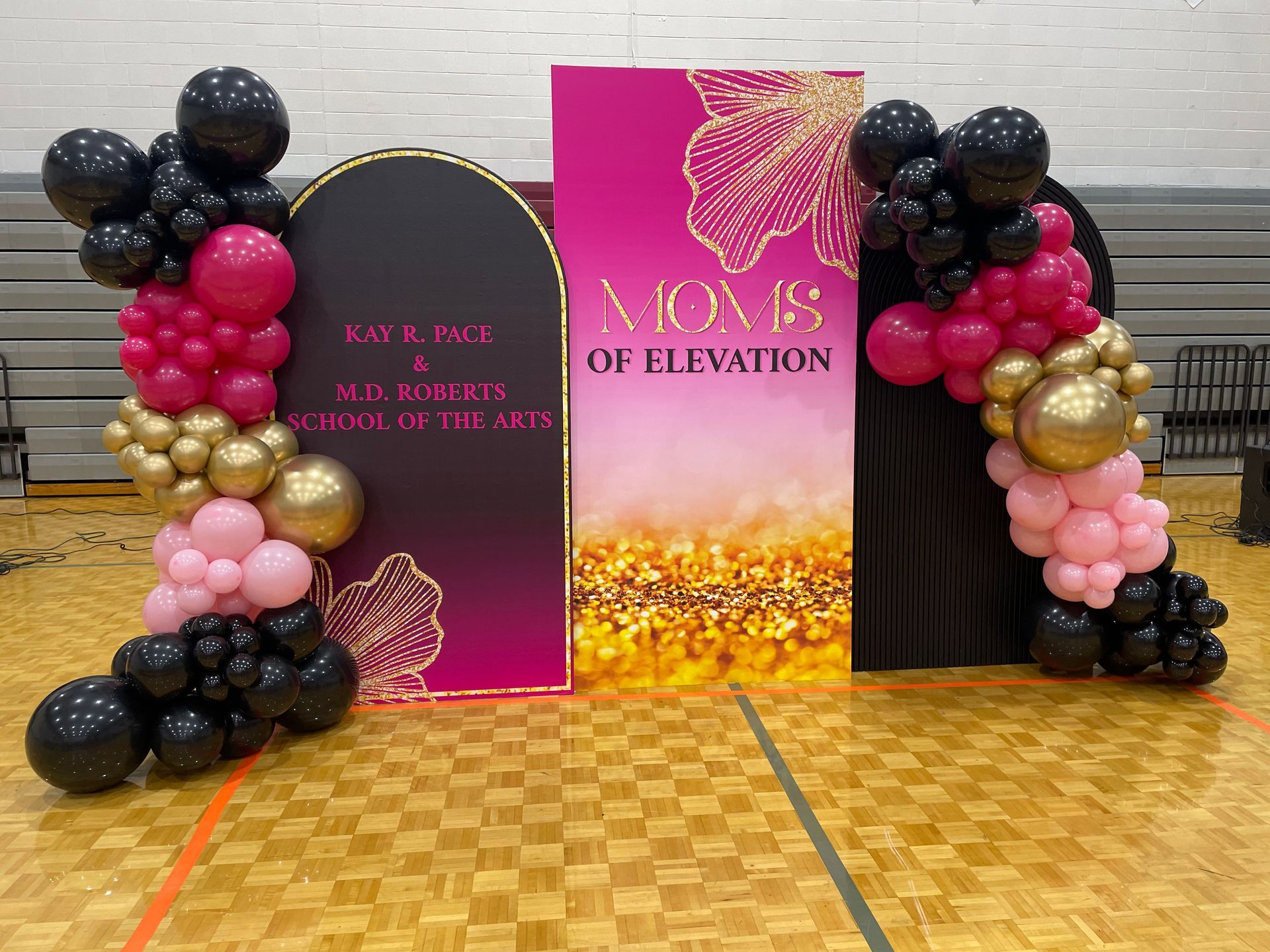 Black pink and gold balloon columns framing branded step and repeat backdrop for school or women’s event