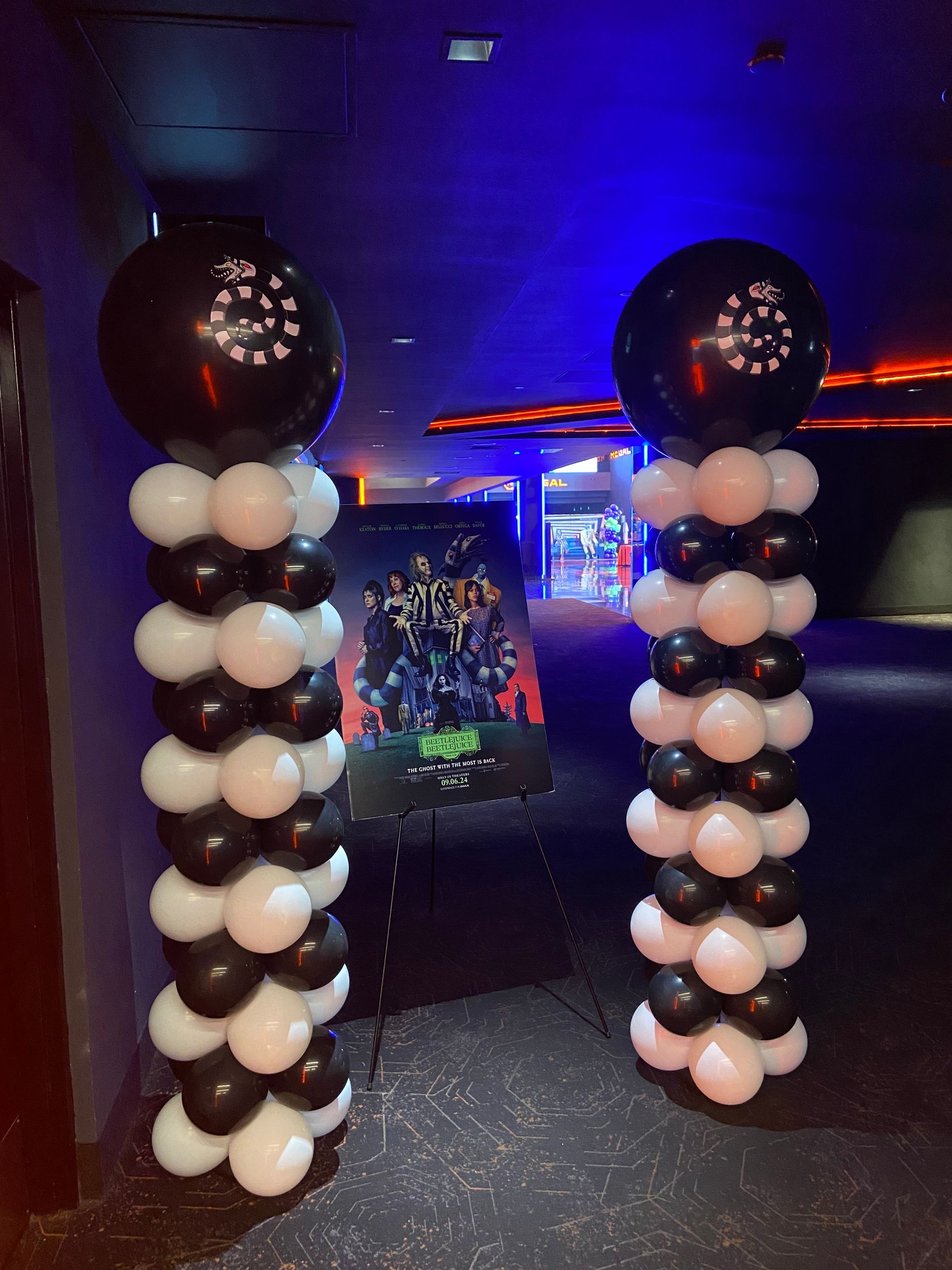 Black and white balloon columns with large topper balloons inside a neon-lit event venue hallway
