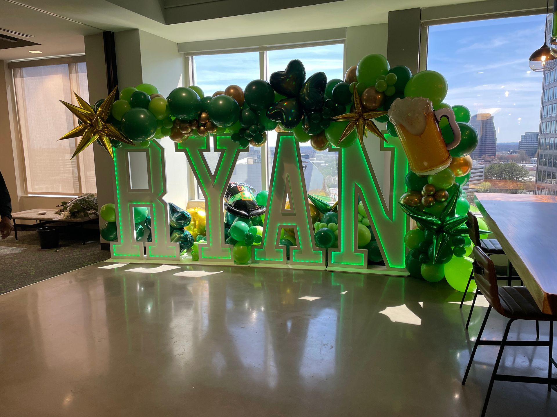 Large illuminated marquee letters with green and gold balloon garland for milestone birthday celebration