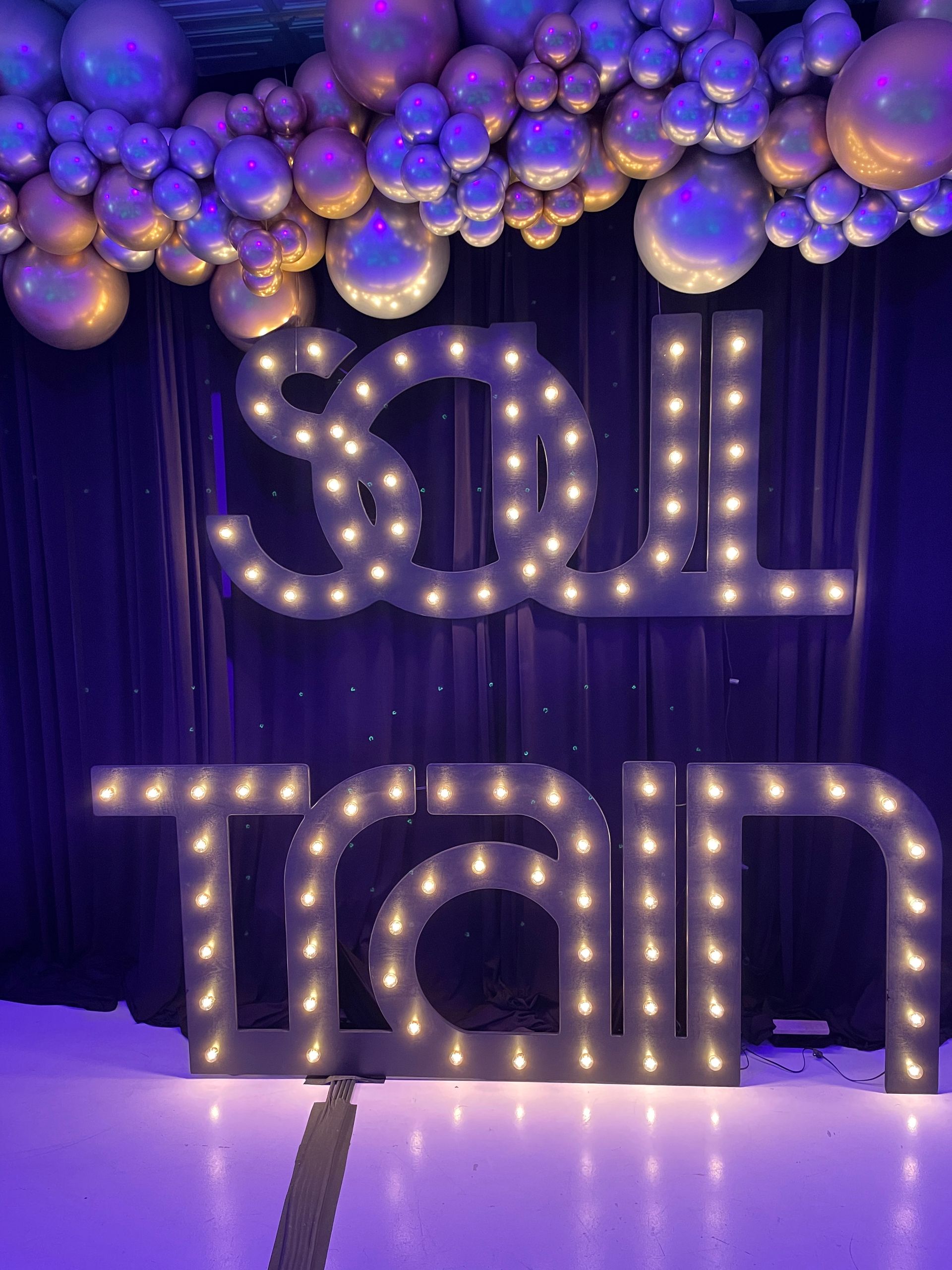 Marquee SOUL letters with metallic purple balloon garland and dramatic lighting backdrop