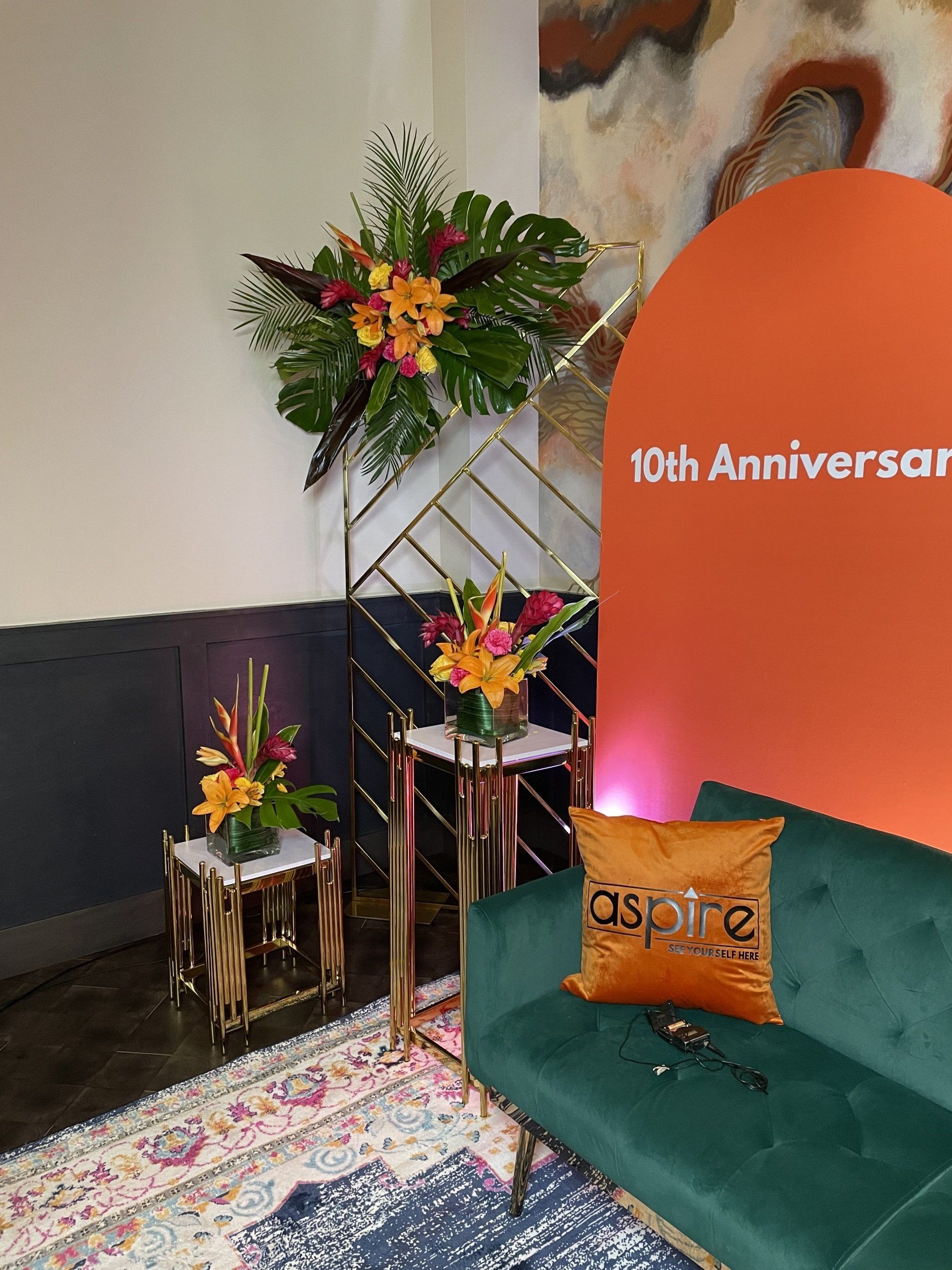 Colorful floral arrangement displayed on a gold stand beside a custom event backdrop