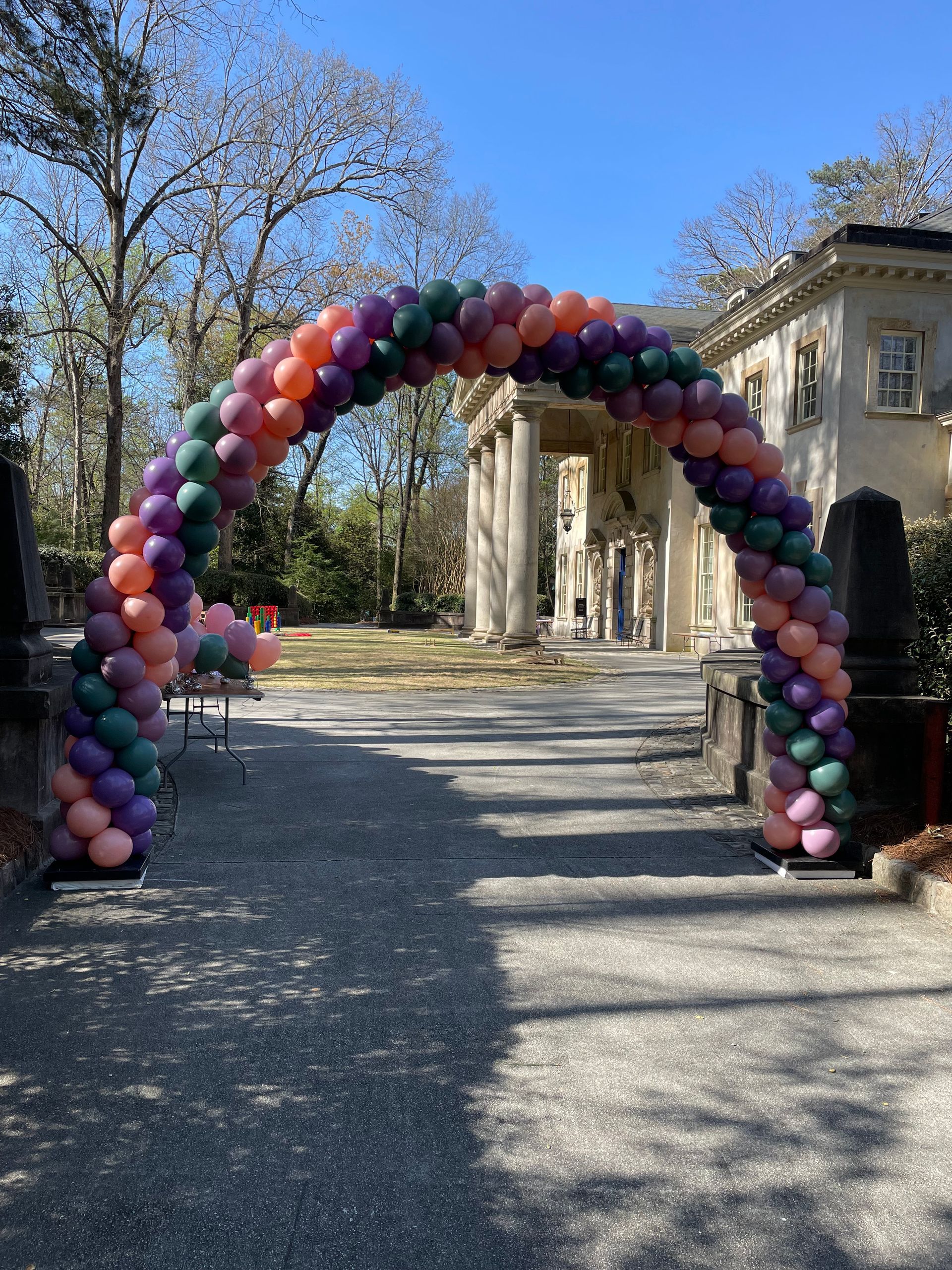 Multicolor balloon arch outdoor entrance setup near a historic building and garden