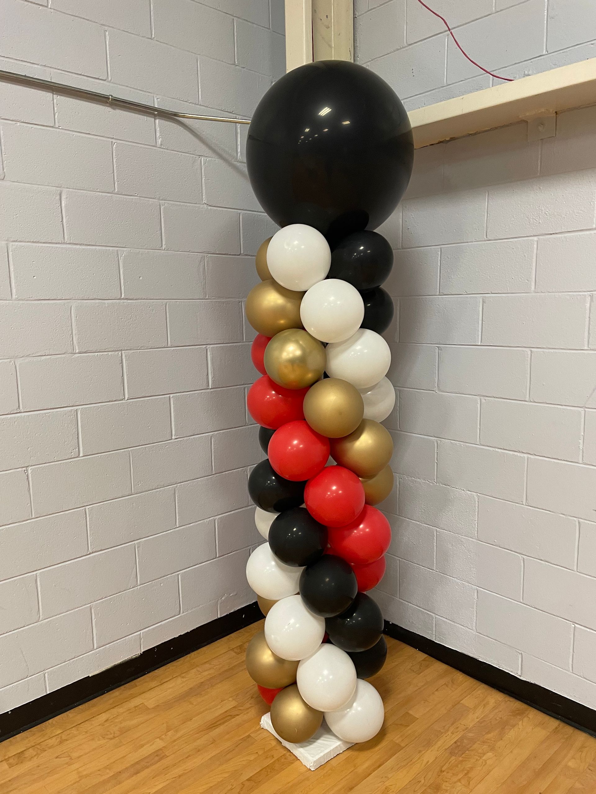 Black, white, and gold balloon column with oversized black topper balloon indoors
