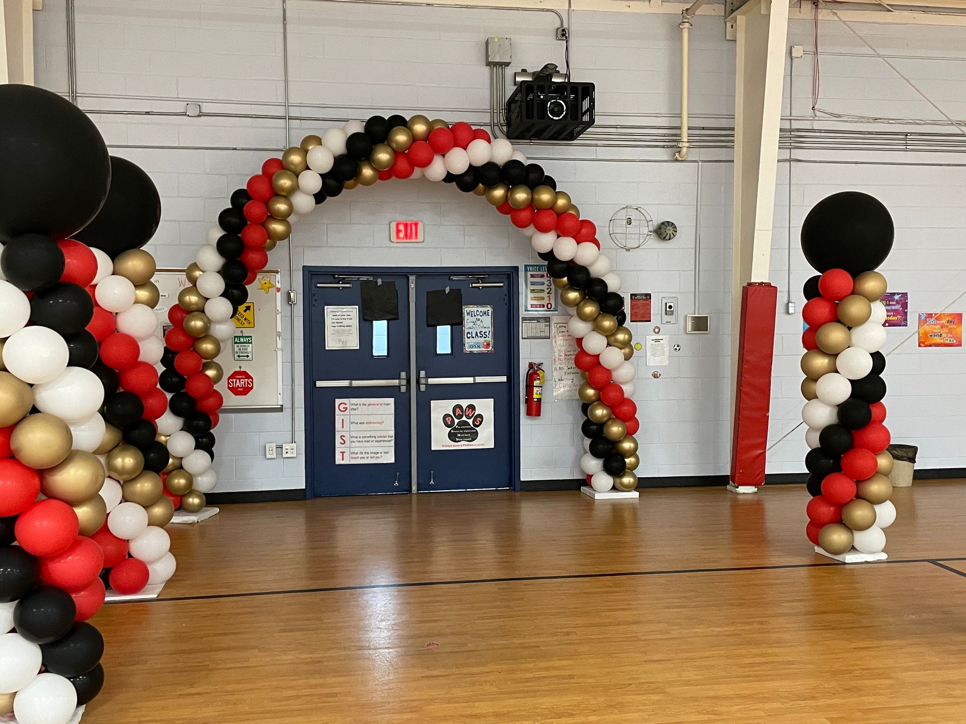 Black, gold, and red balloon arch and columns decorating a gym or event hall entrance
