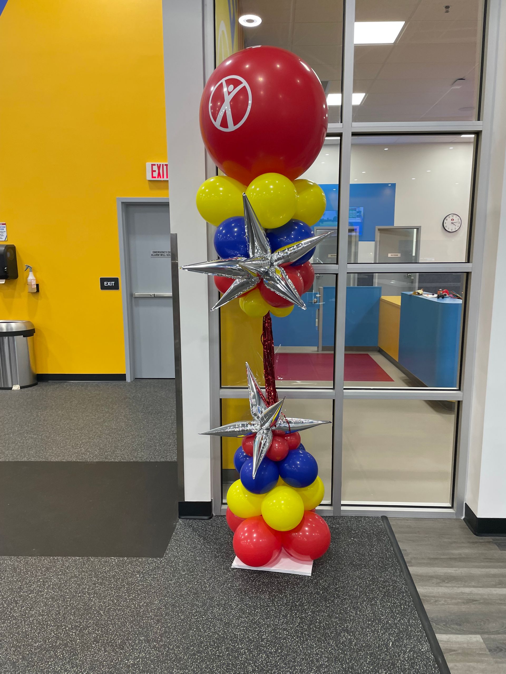 Red, yellow, and blue balloon column with silver star topper inside a bright office space