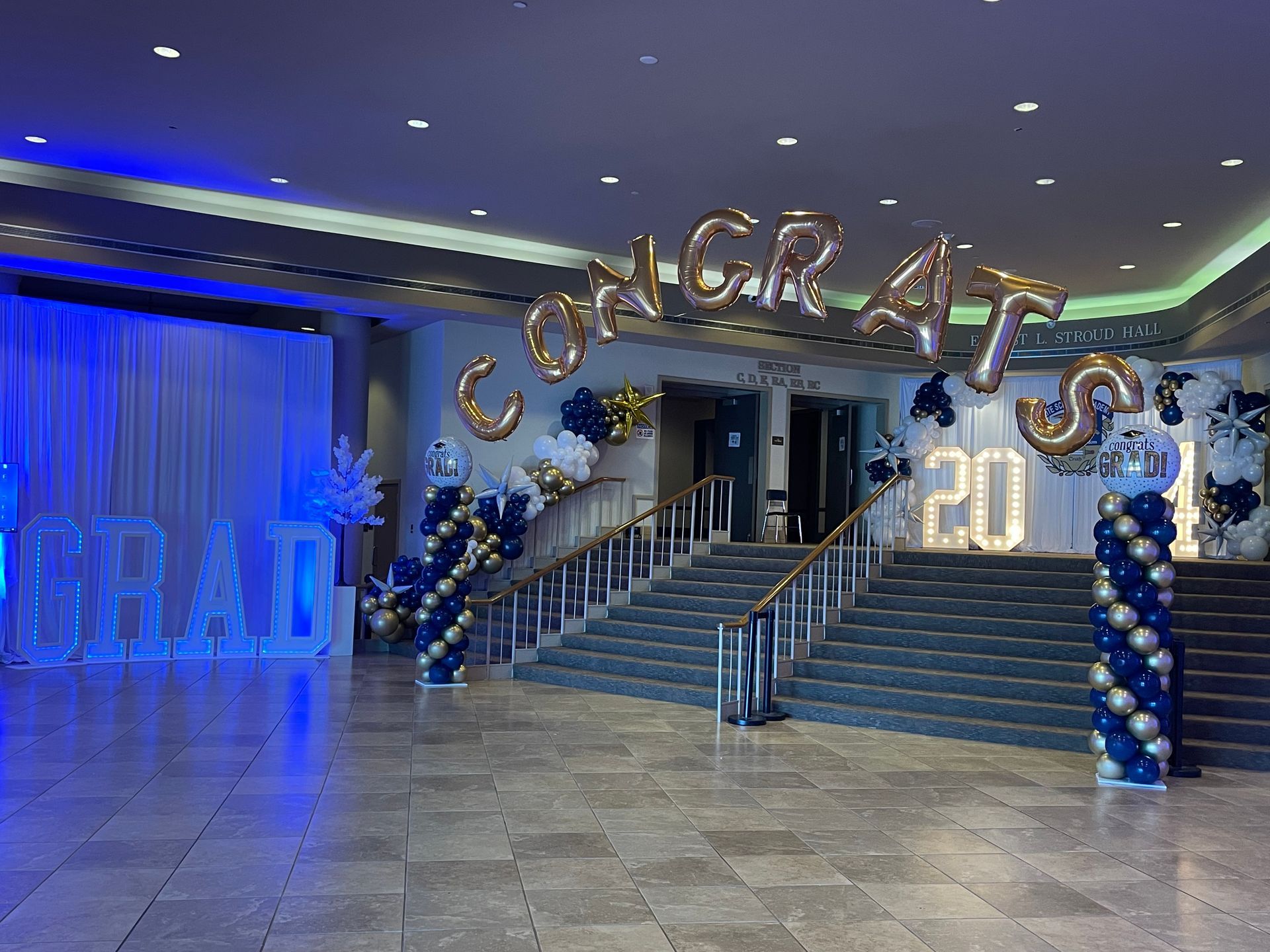 Graduation balloon décor with blue and gold arches and “Congrats” balloons at an indoor staircase