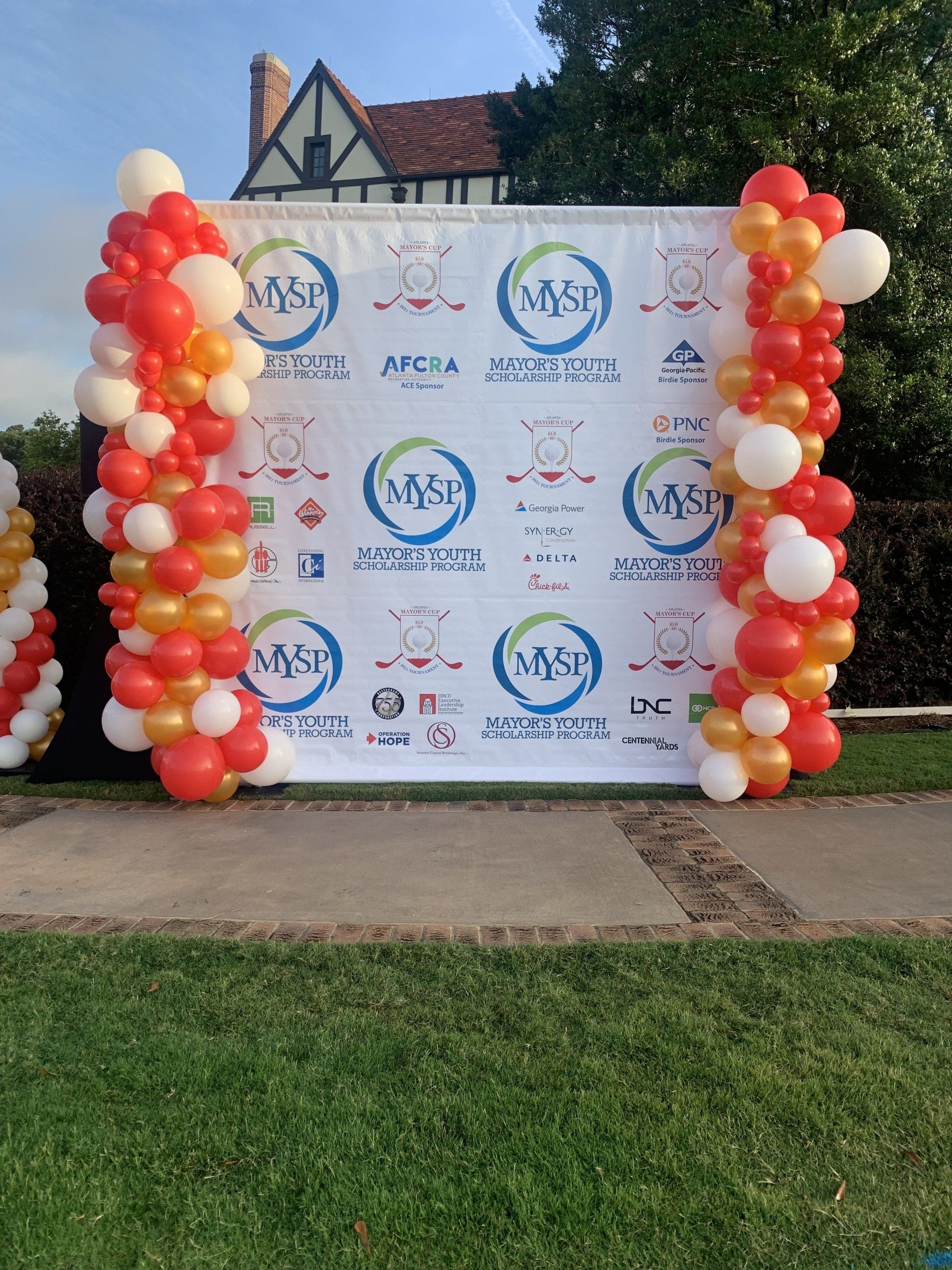 Red white and gold balloon columns framing branded step and repeat backdrop for outdoor corporate event