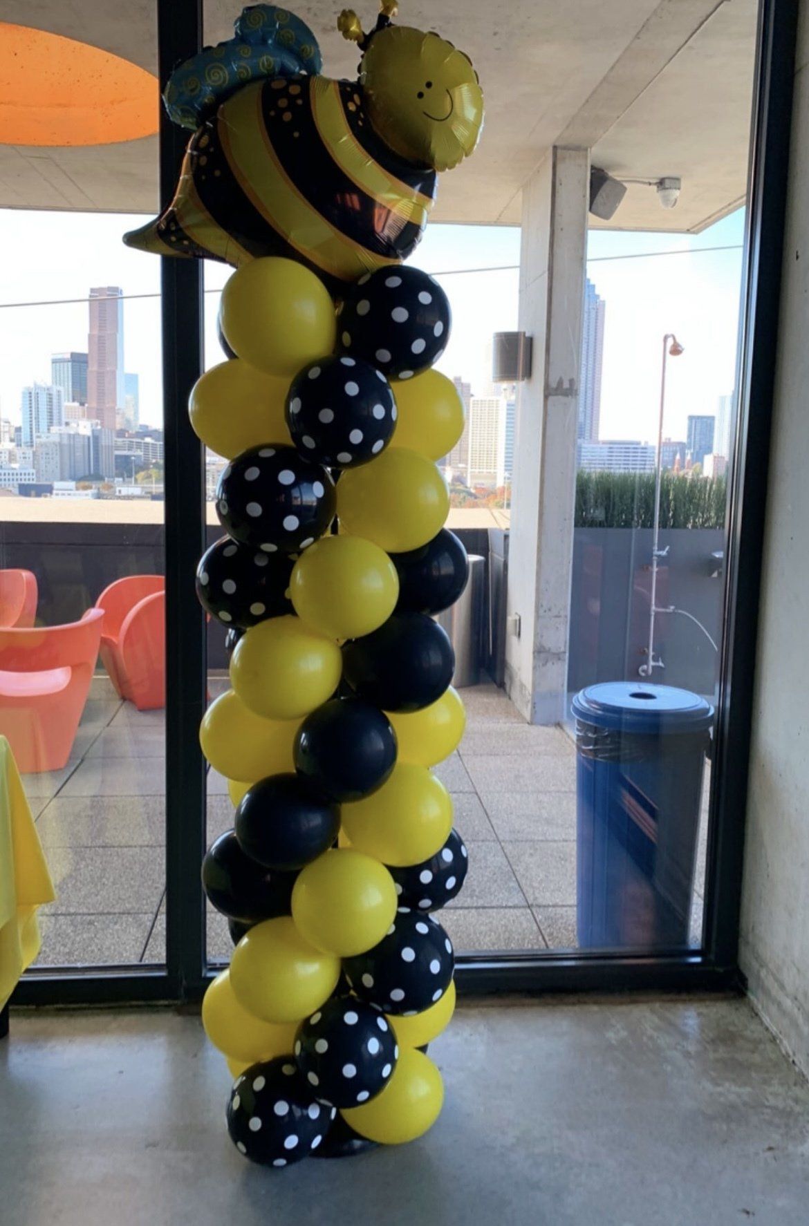 Yellow and black balloon column with bee-shaped foil topper inside an event space with city view