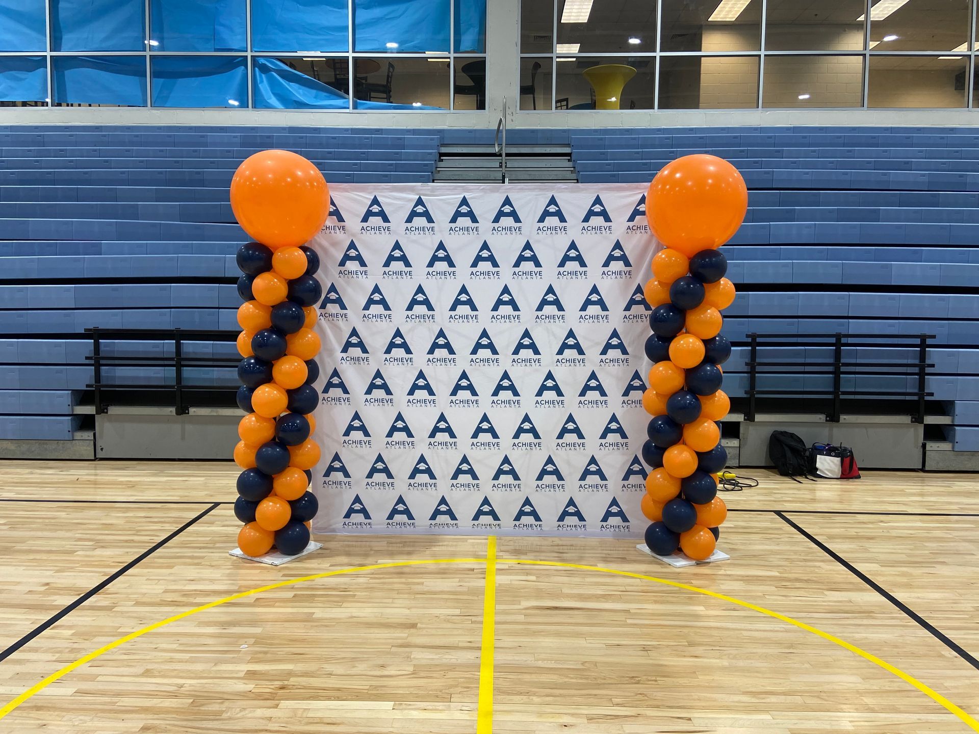Orange and navy balloon columns set up in a gym with a step-and-repeat backdrop