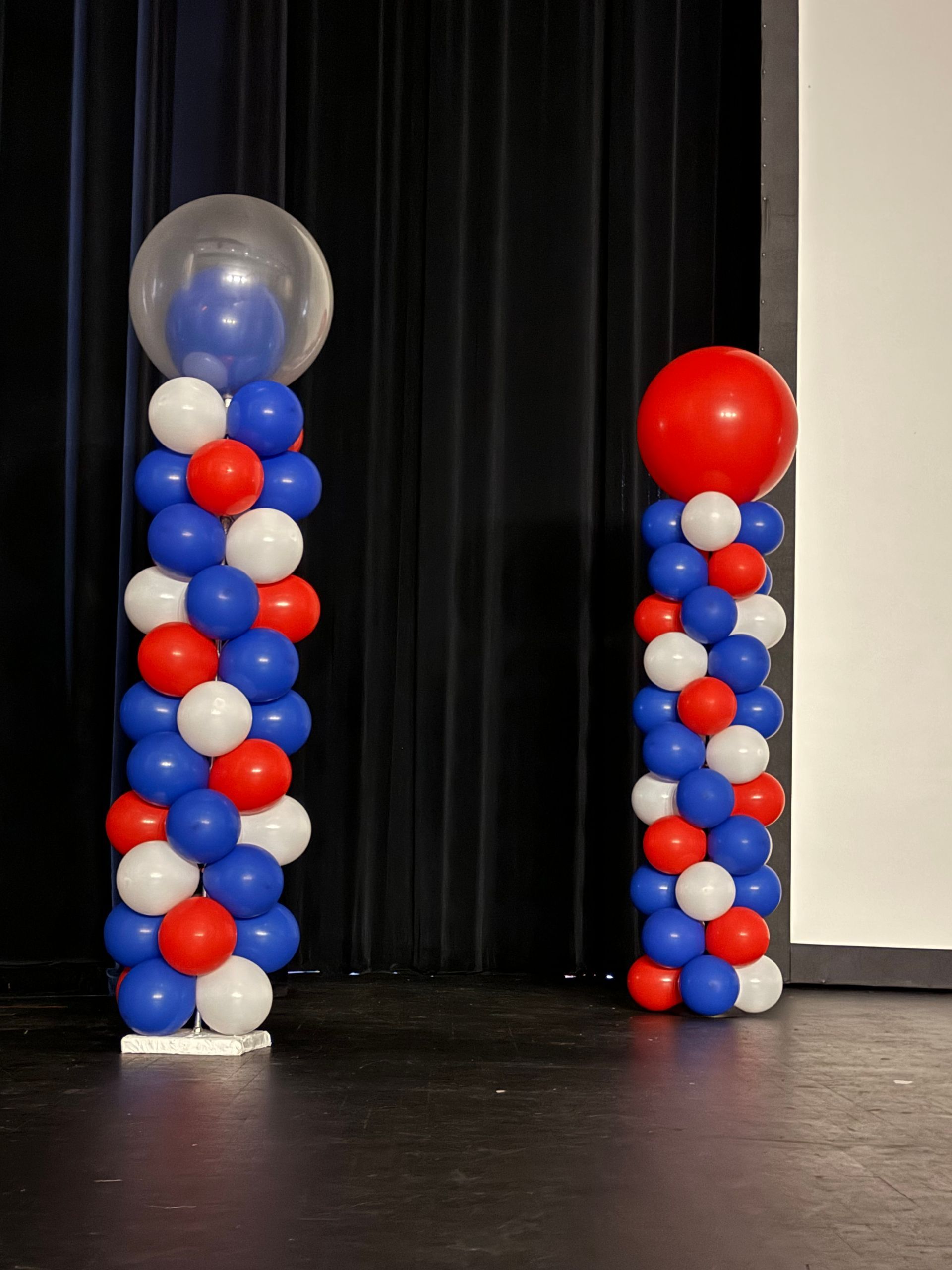 Red, white, and blue balloon columns set against a black curtain backdrop for an indoor event