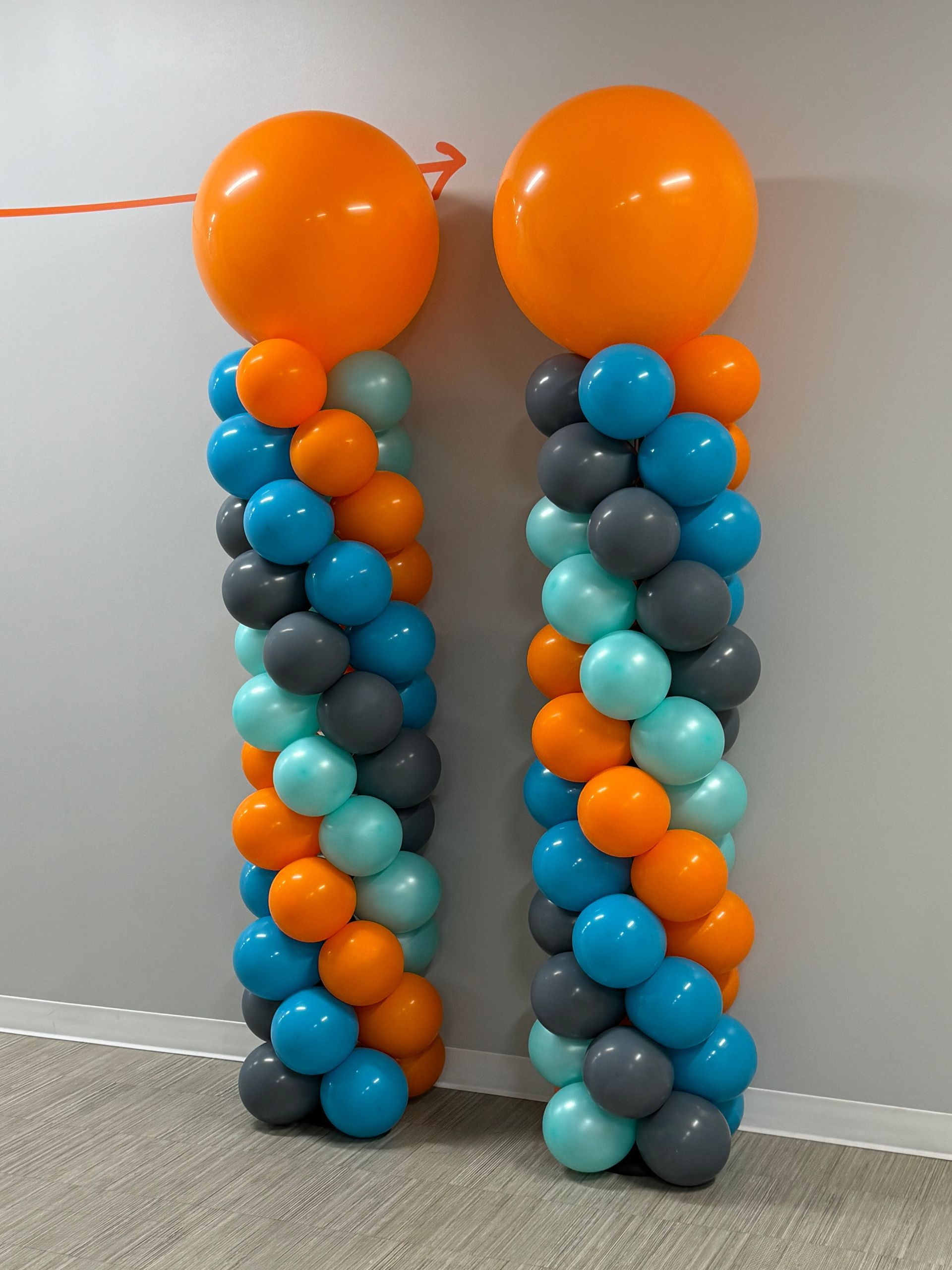Orange and teal balloon columns with oversized topper balloons for a party setup