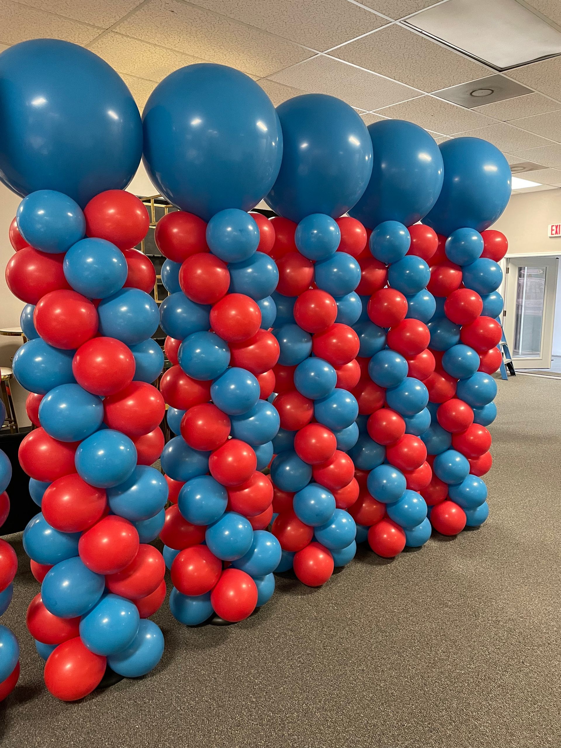Red and blue balloon wall backdrop with oversized blue topper balloons for an indoor event