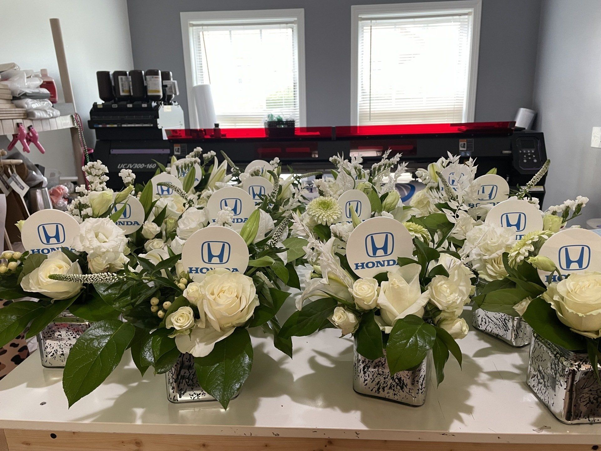 White rose floral arrangements with branded Honda logos displayed on a preparation table