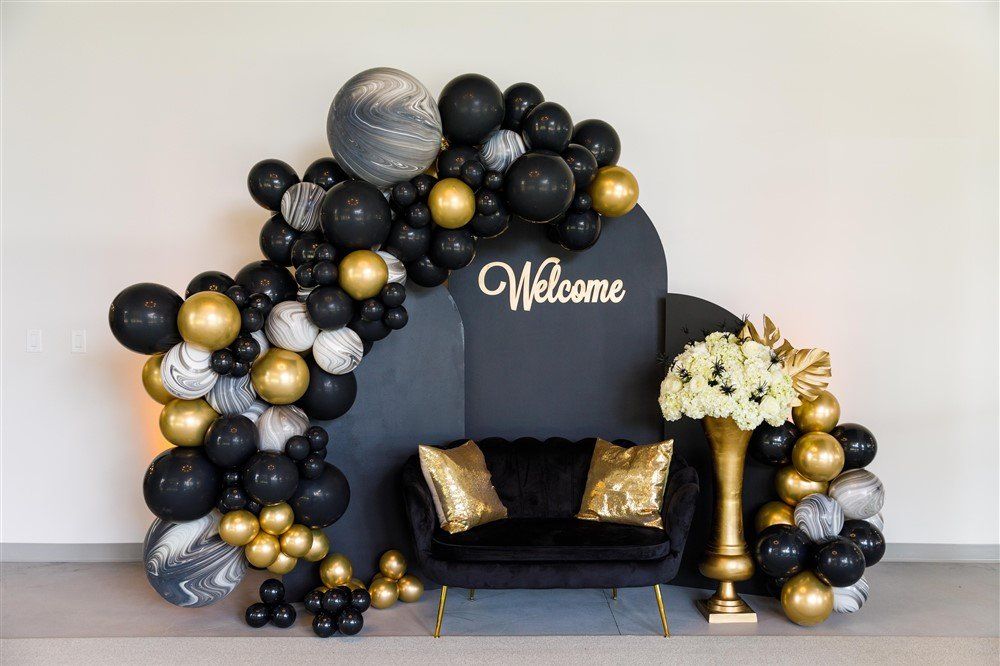 Black and gold organic balloon arch with welcome sign and lounge seating for luxury celebration