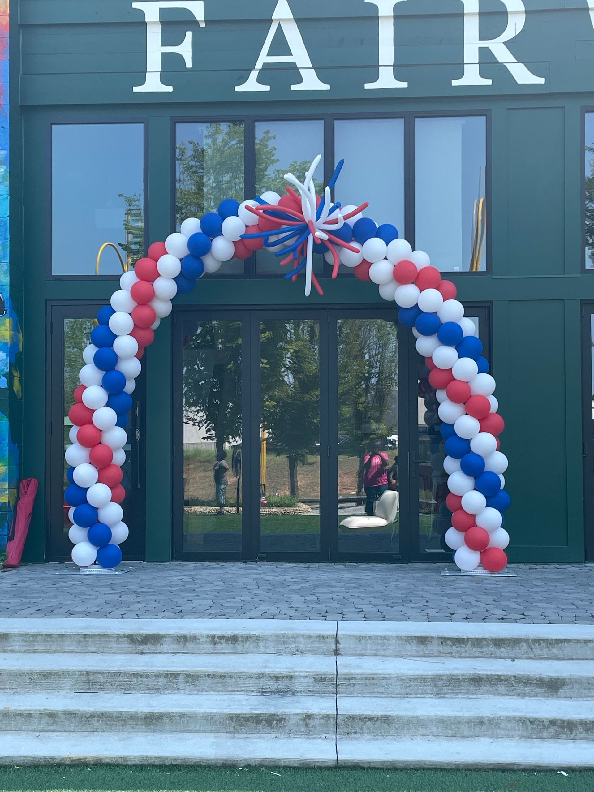 Red, white, and blue balloon arch outside a building entrance for a patriotic themed event