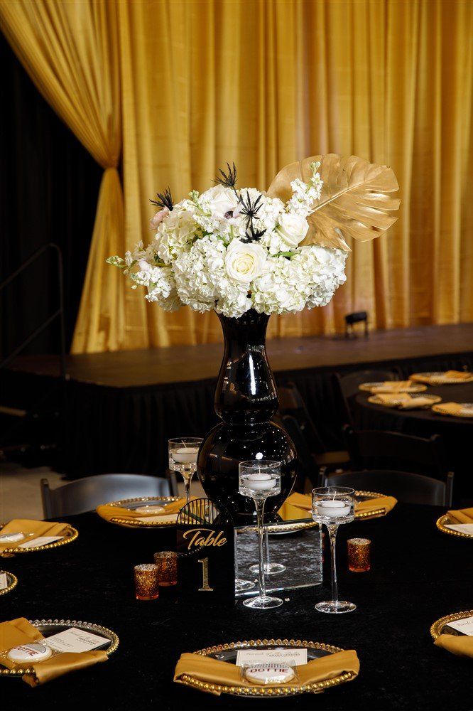 White floral arrangement with gold decorative leaves styled in front of gold draped curtains
